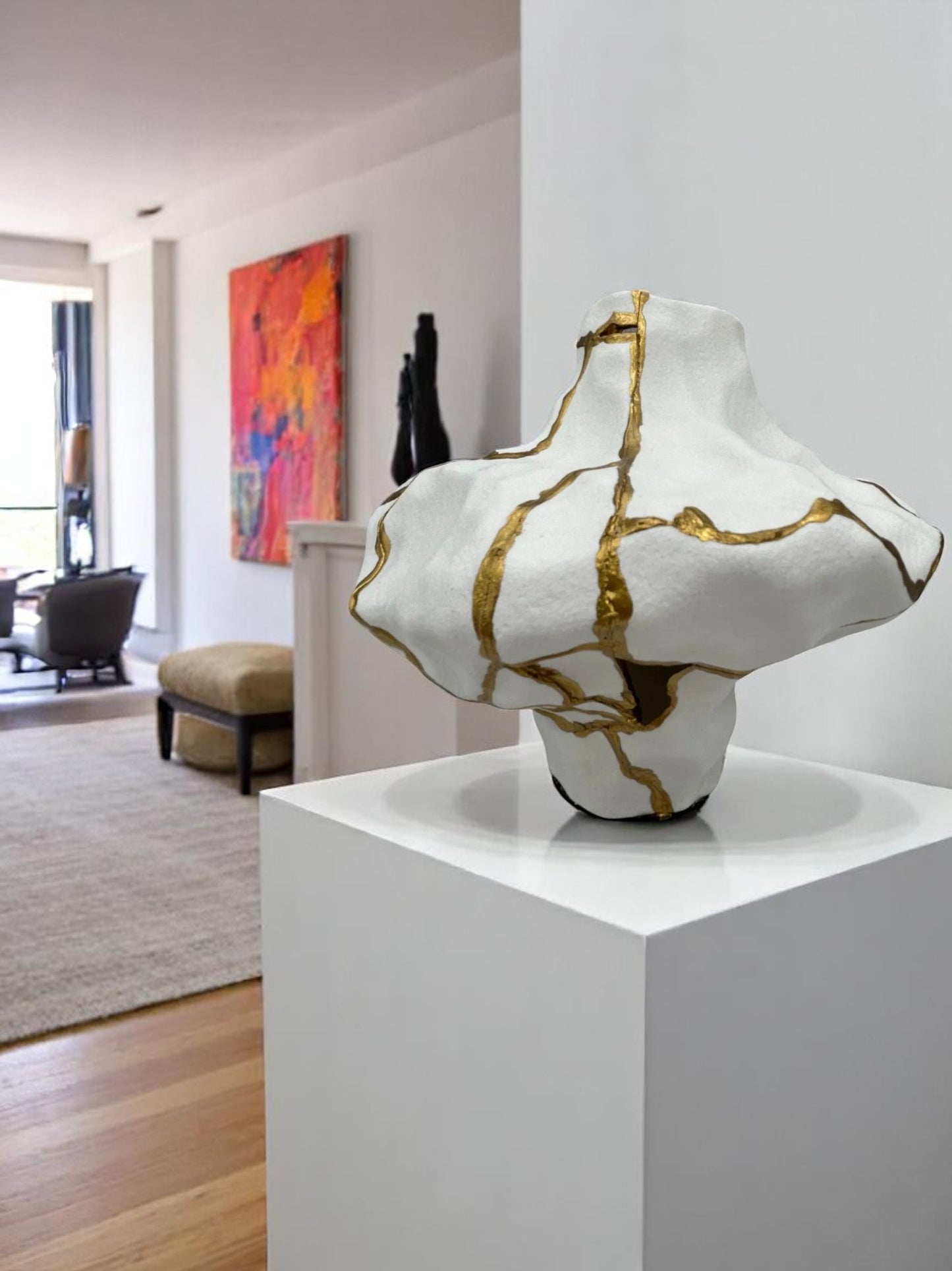 Abstract white ceramic sculpture with gold repair lines displayed on white pedestal in modern living space