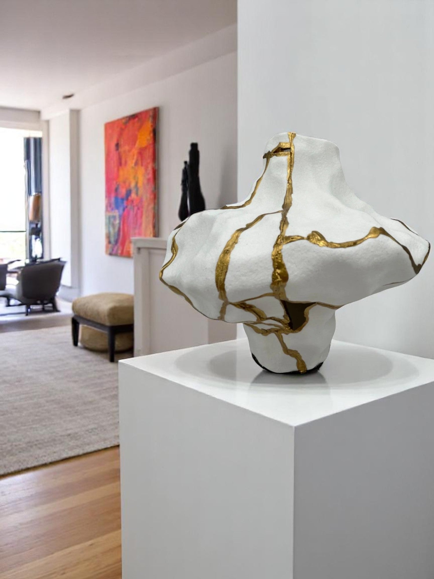 Abstract white ceramic sculpture with gold repair lines displayed on white pedestal in modern living space