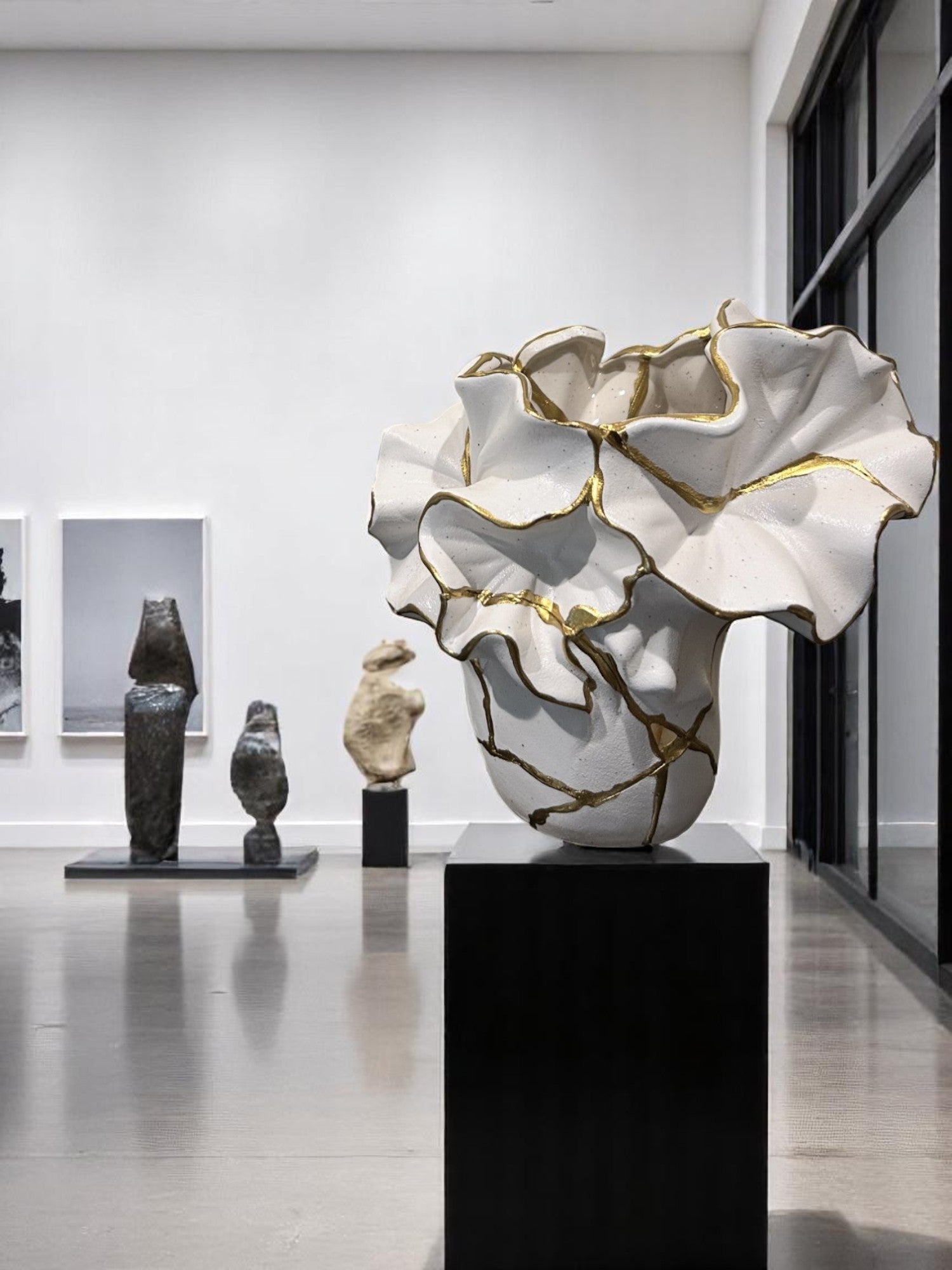 Abstract white ceramic sculpture with gold accents displayed on black pedestal in a modern gallery setting