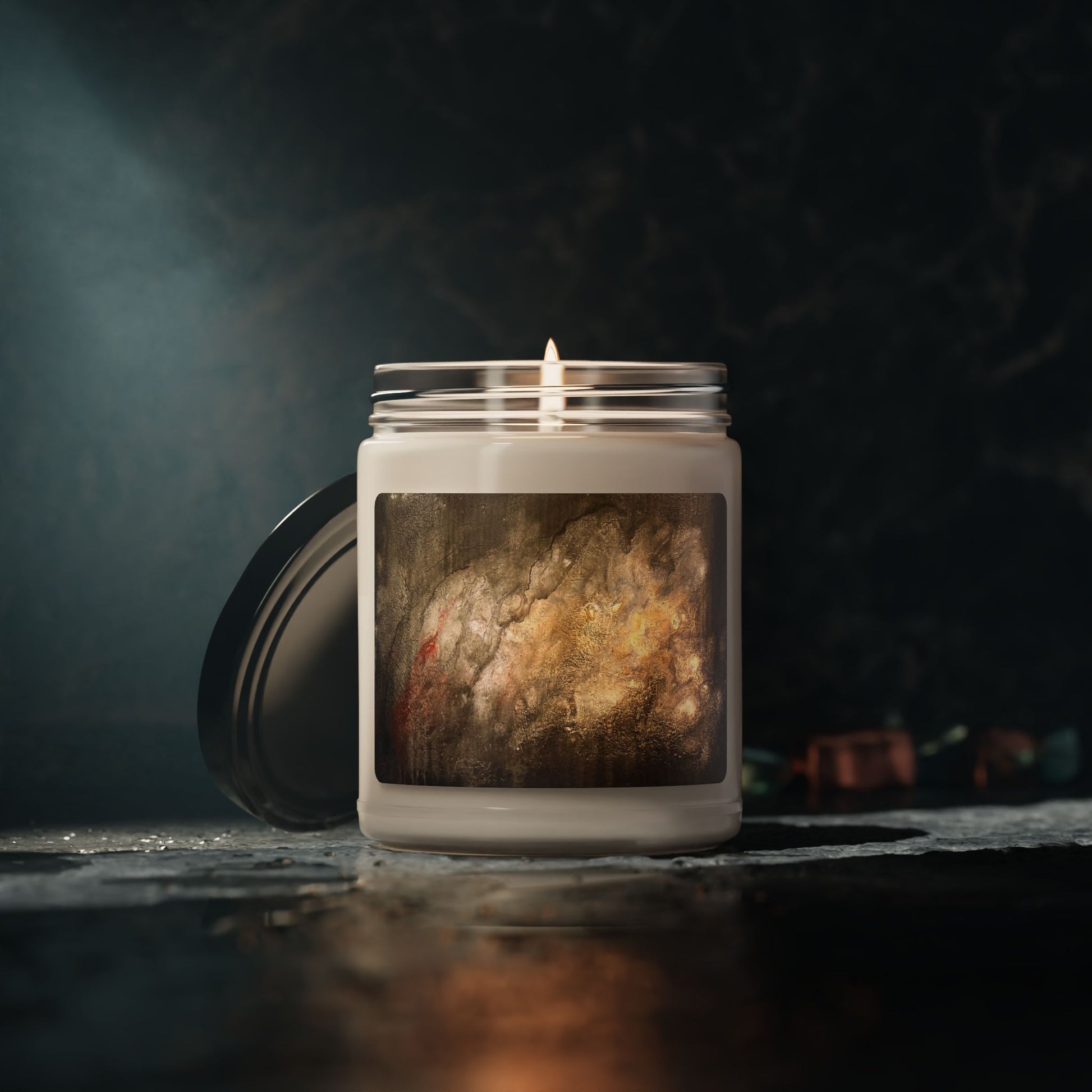 Lit 9oz soy candle in frosted glass jar with abstract painting label by Ben Woolfitt, dark moody background.
