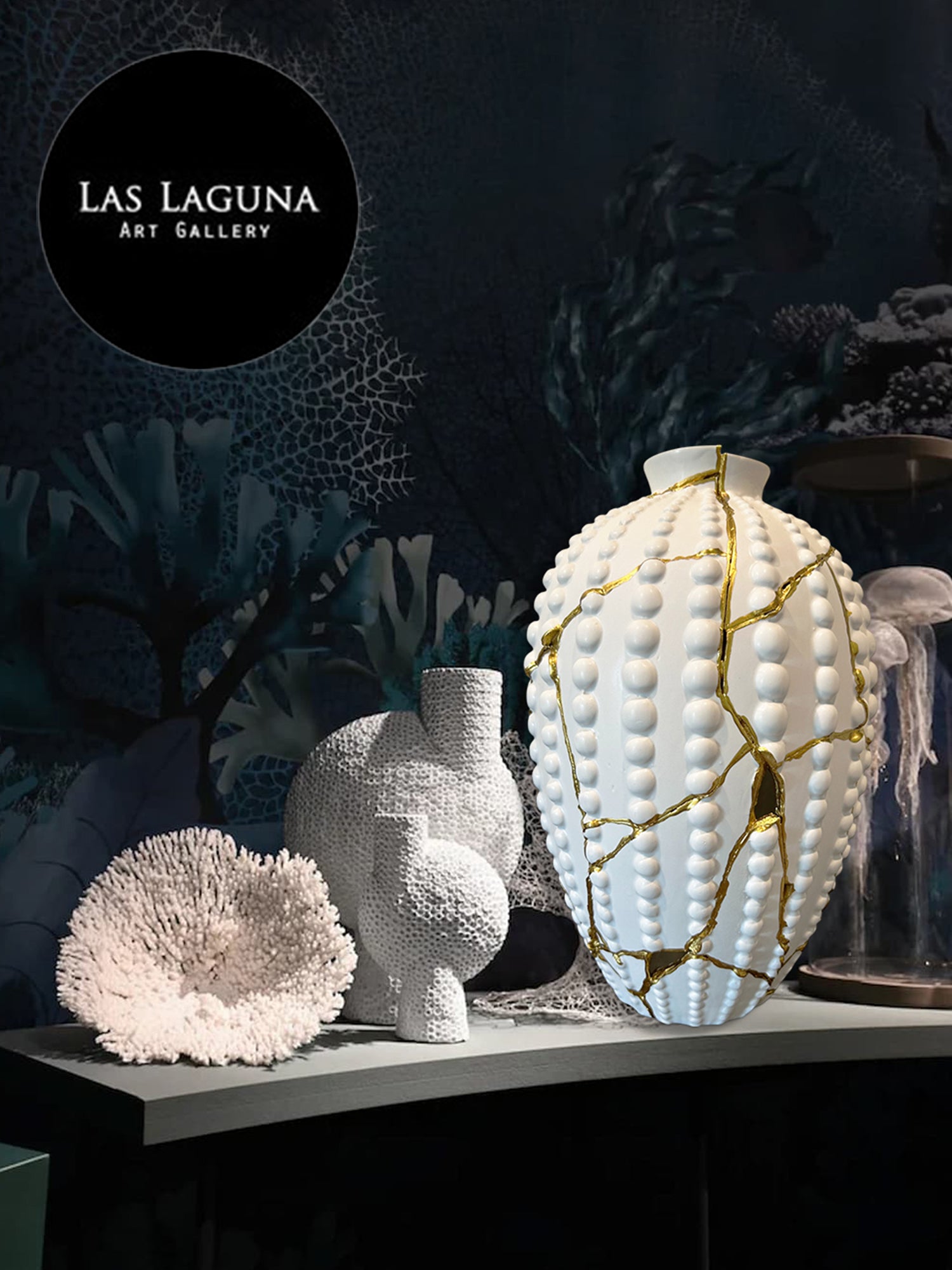 White ceramic sea urchin vase with gold repair lines, coral sculpture, and textured ceramic piece on dark gallery shelf
