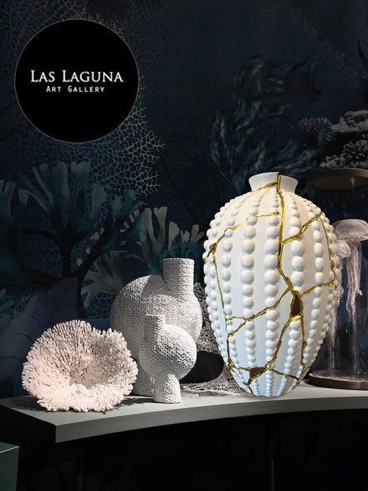 White ceramic sea urchin vase with gold repair lines, coral sculpture, and textured ceramic piece on dark gallery shelf