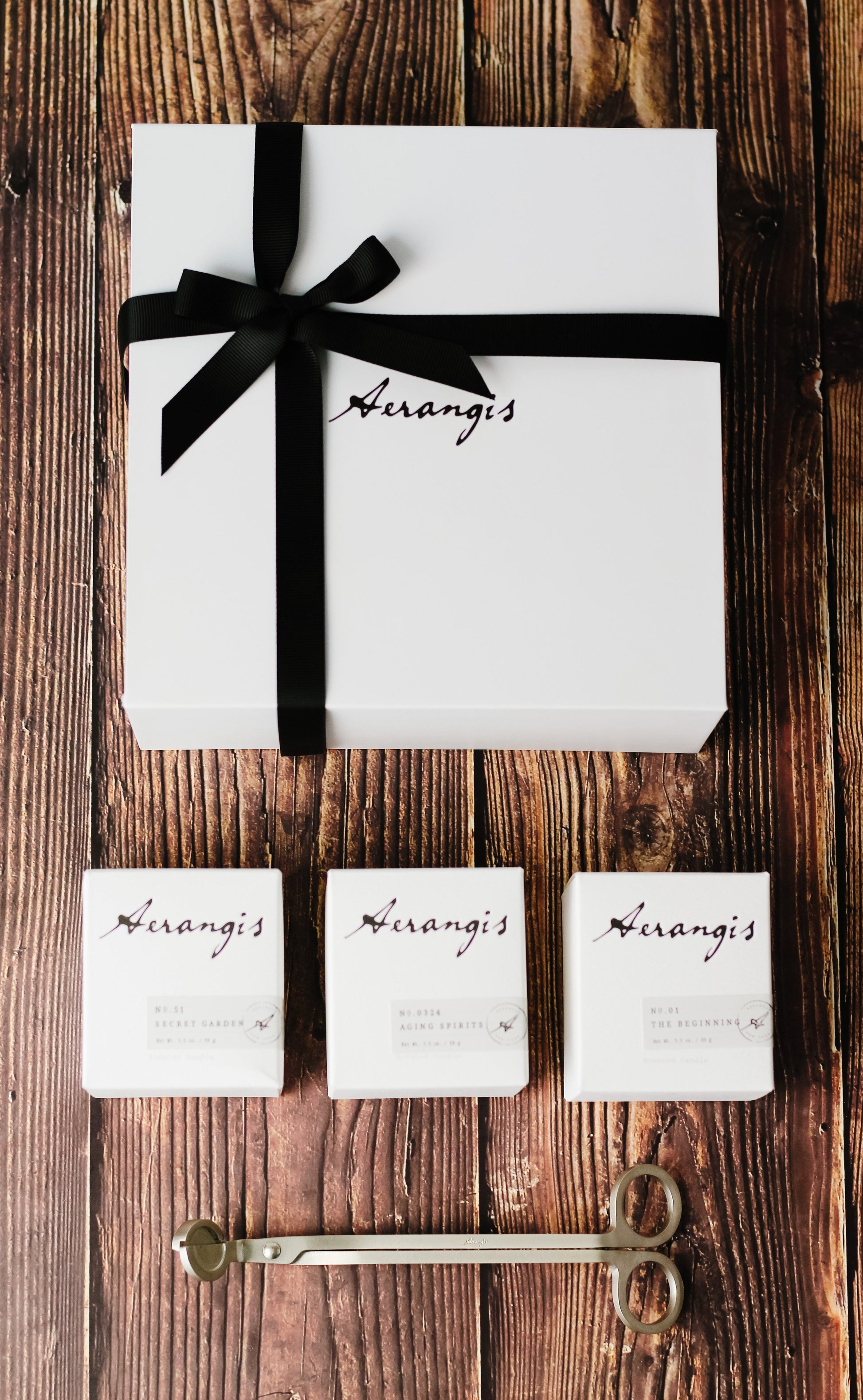 Aerangis Discovery Journey Gift Set with three mini candles and black ribbon on white box, rustic wood background