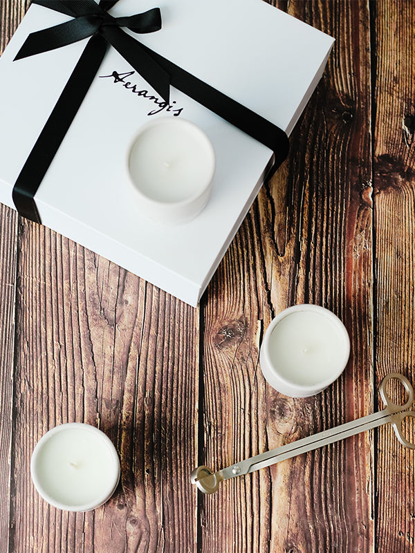 White Aerangis Discovery Journey Gift Set box with black ribbon, three small white candles, and gold candle snuffer on wood table