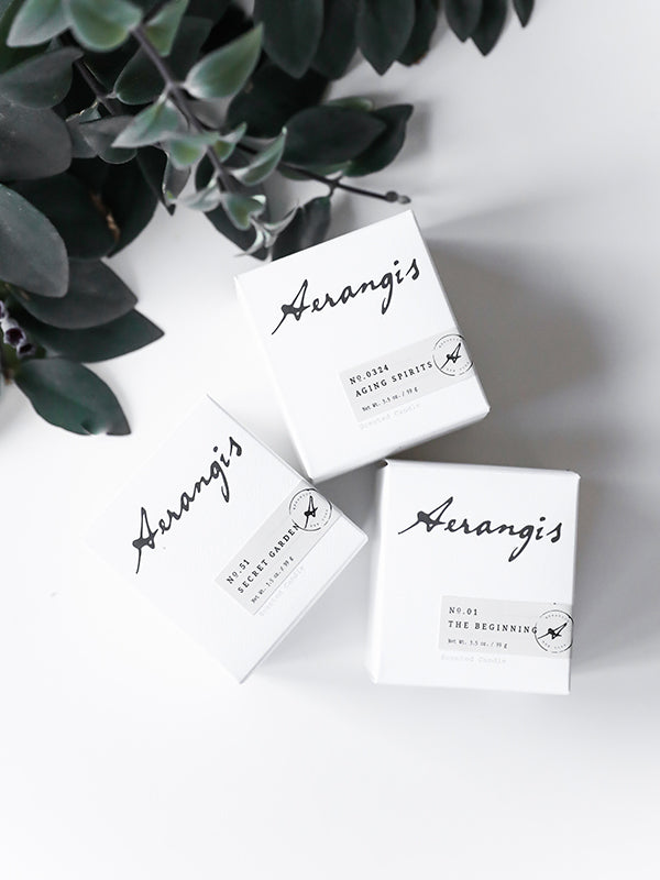 Three white Aerangis Discovery Journey gift set boxes with black script text on a white surface next to green leaves
