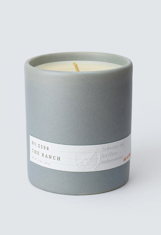 Gray ceramic candle labeled Aerangis No. 2598 The Ranch with tobacco, leather, and cedarwood scent notes on white background