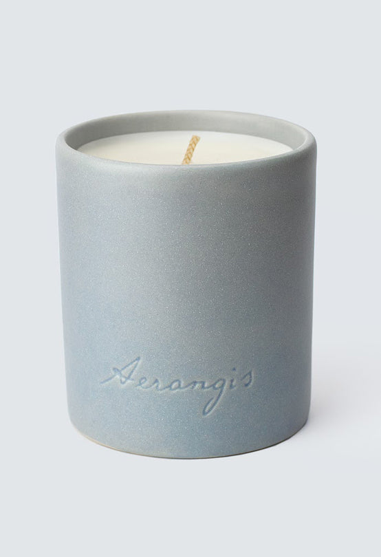Light blue ceramic candle holder with Aerangis logo, filled with white wax candle on a plain light background