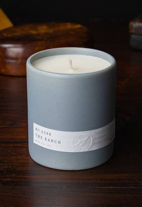 Matte gray ceramic candle labeled Aerangis No. 2598 The Ranch, unlit with white wax inside on wooden surface