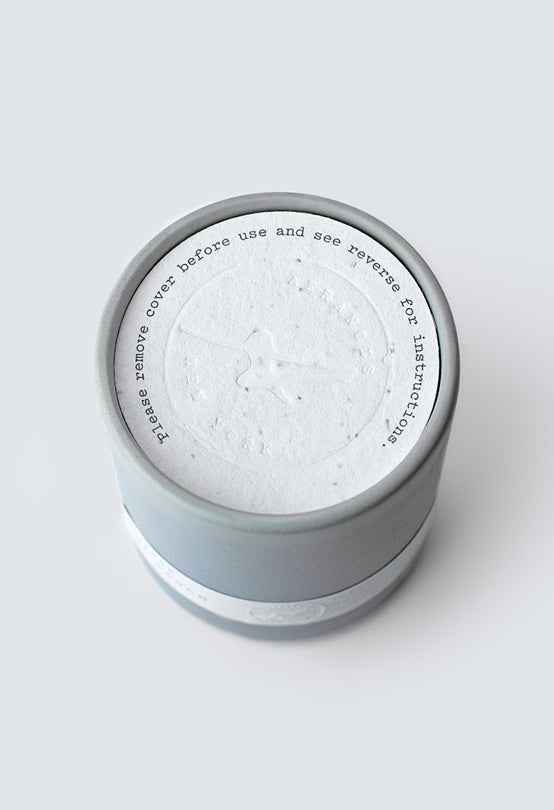 Gray cylindrical container with textured white lid featuring embossed logo and printed instructions on top