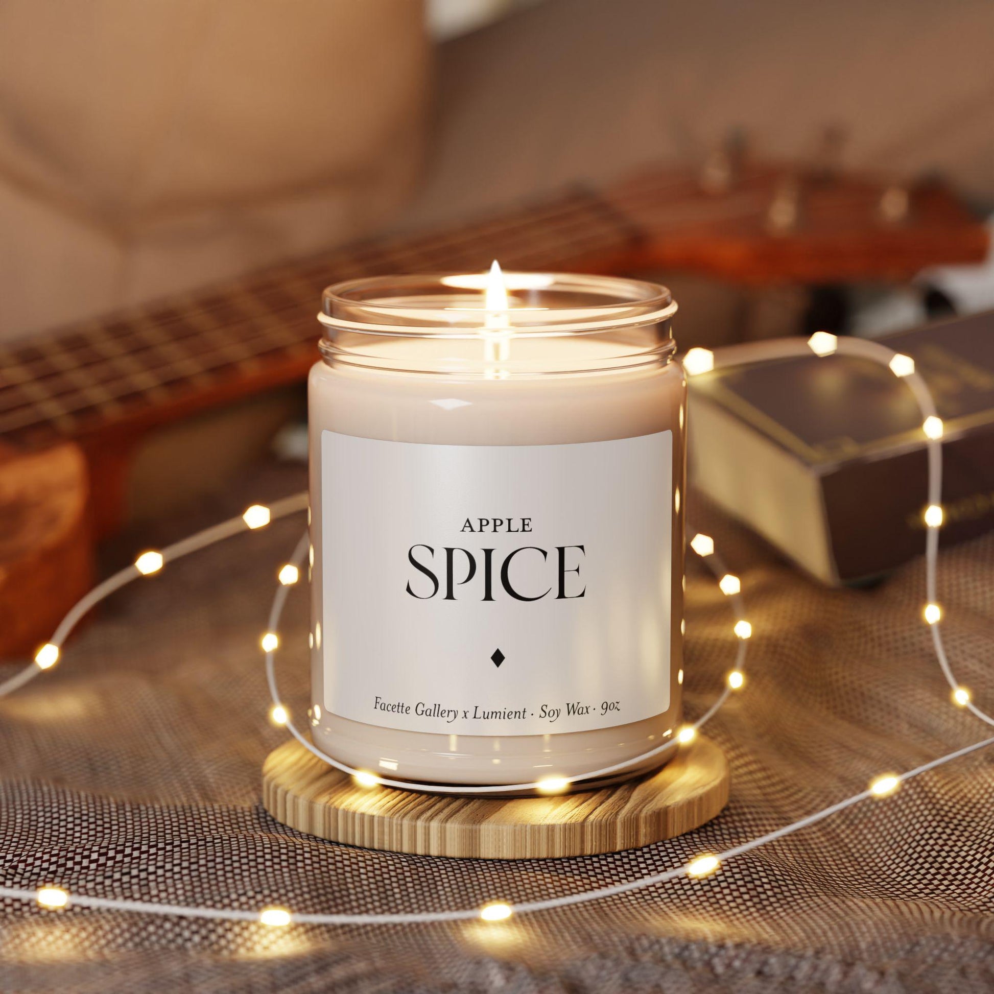 Lit Apple Spice scented soy candle in clear glass jar with white label on wooden coaster surrounded by fairy lights