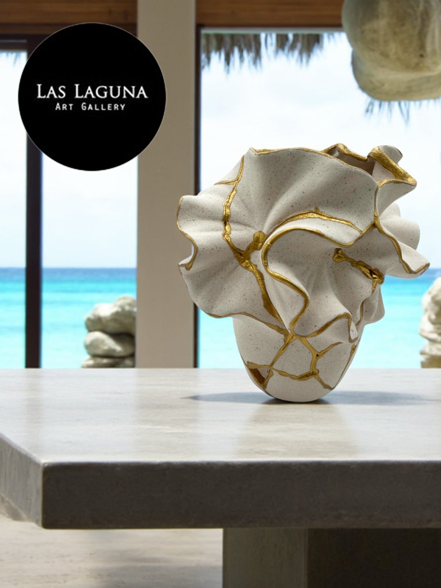 Ceramic vase with organic ruffled design and gold repair accents displayed on light stone table by ocean view window