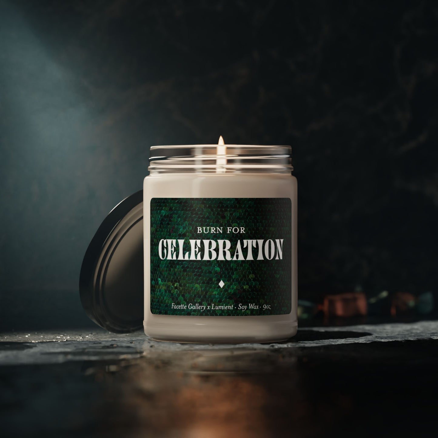 Lit 9oz soy candle in glass jar with green sequin label reading "Burn for Celebration" and black lid beside it
