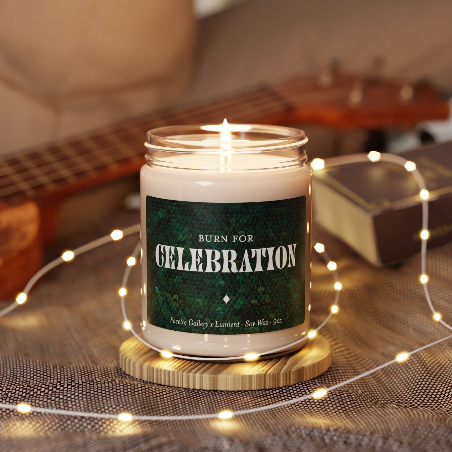 Lit Celebration candle in glass jar with green sequin label, soy wax, 9oz, surrounded by fairy lights on fabric surface