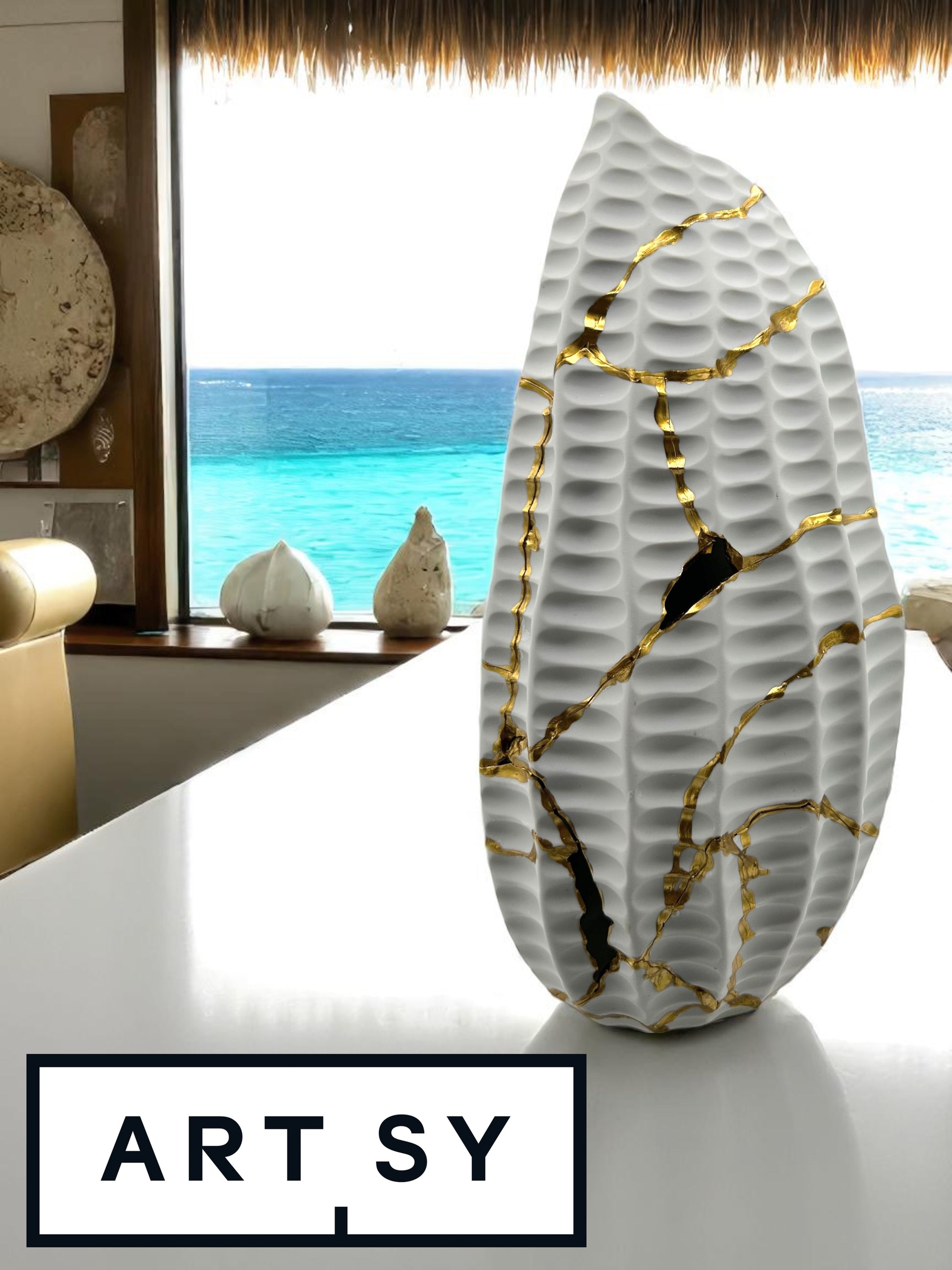 White matte ceramic seahorse vase with gold repair lines on a table, ocean view in background at Facette Gallery