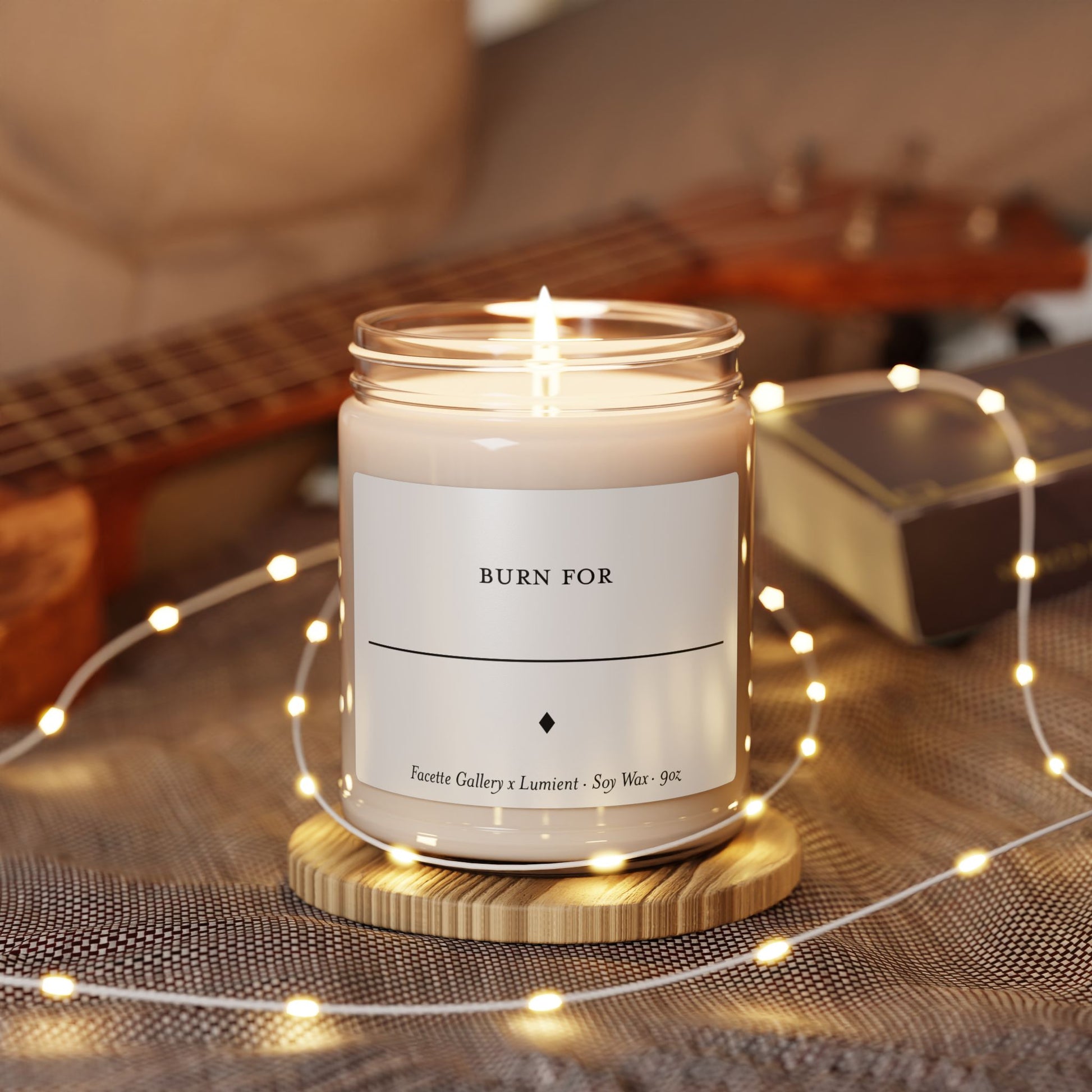 Lit soy candle in 9oz clear glass jar with minimalist white label and black text, placed on wooden coaster with string lights