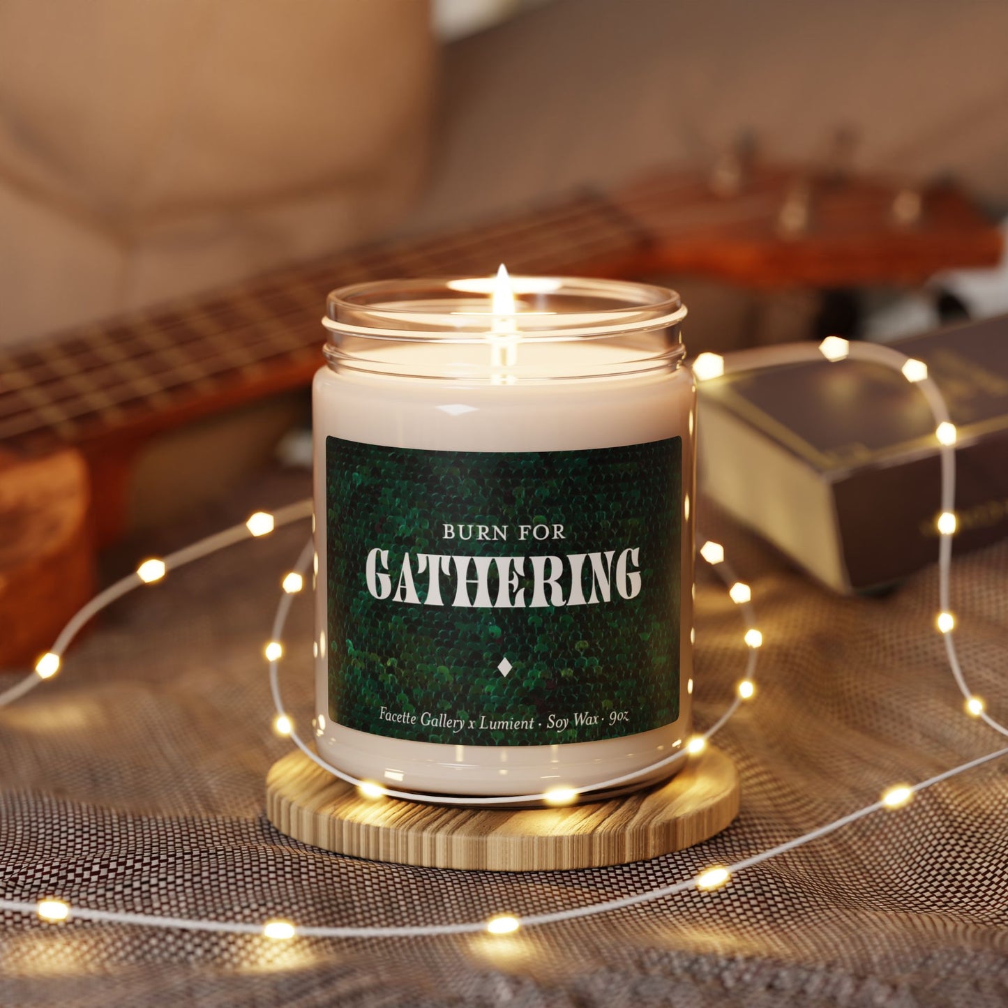 9oz Gathering candle in glass jar with green sequin label, lit with cotton wick on wooden coaster and fairy lights