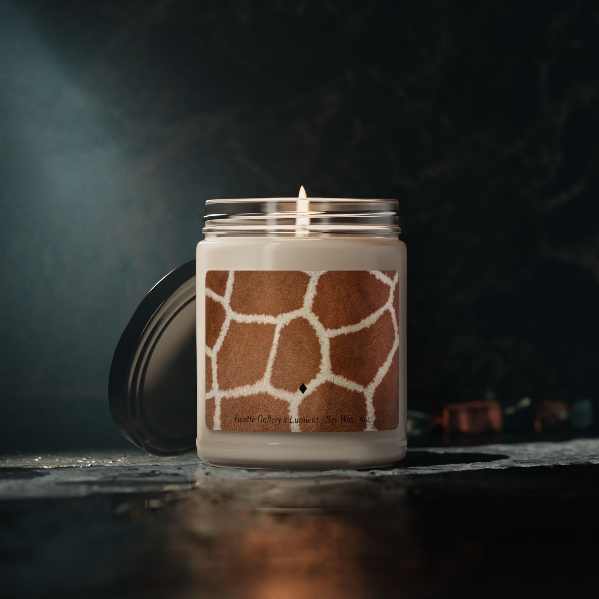 9oz giraffe print soy candle in clear glass jar with black lid, lit wick, on dark textured surface and background