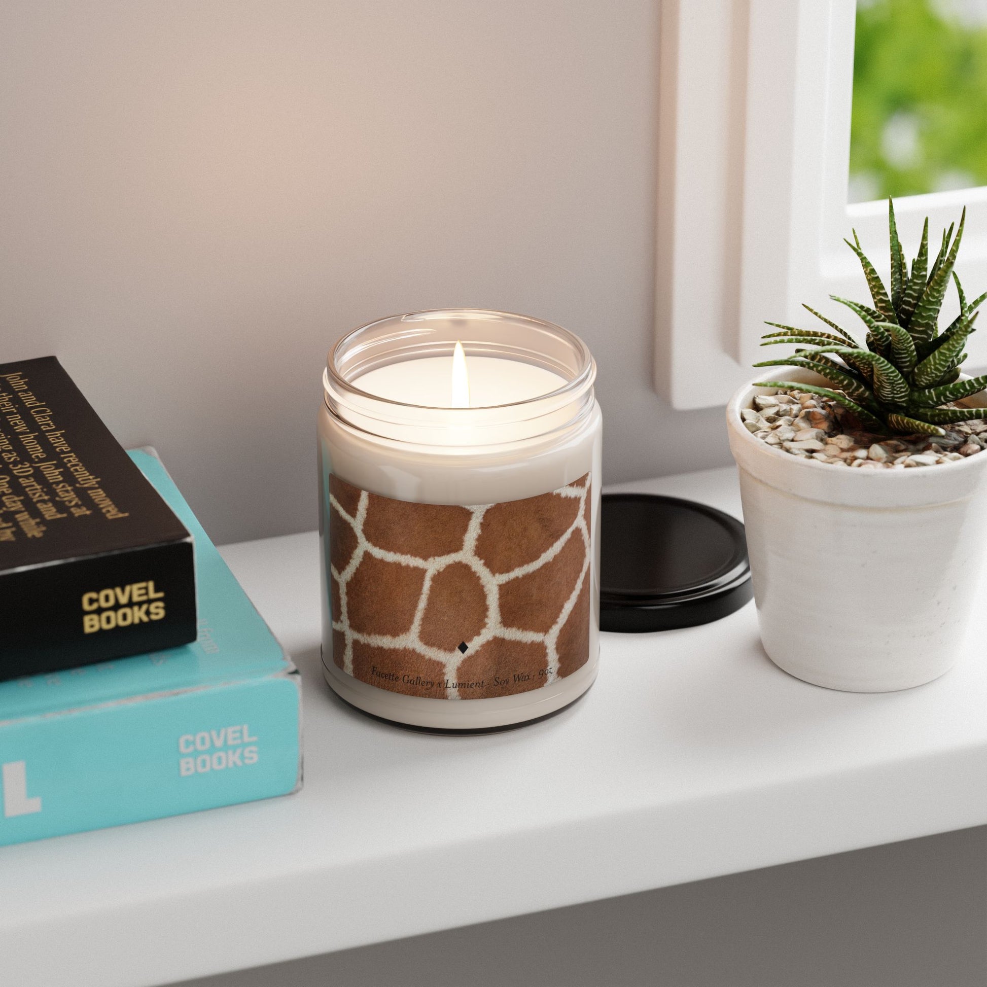 9oz glass jar giraffe print soy candle lit on white windowsill next to potted succulent and stacked books