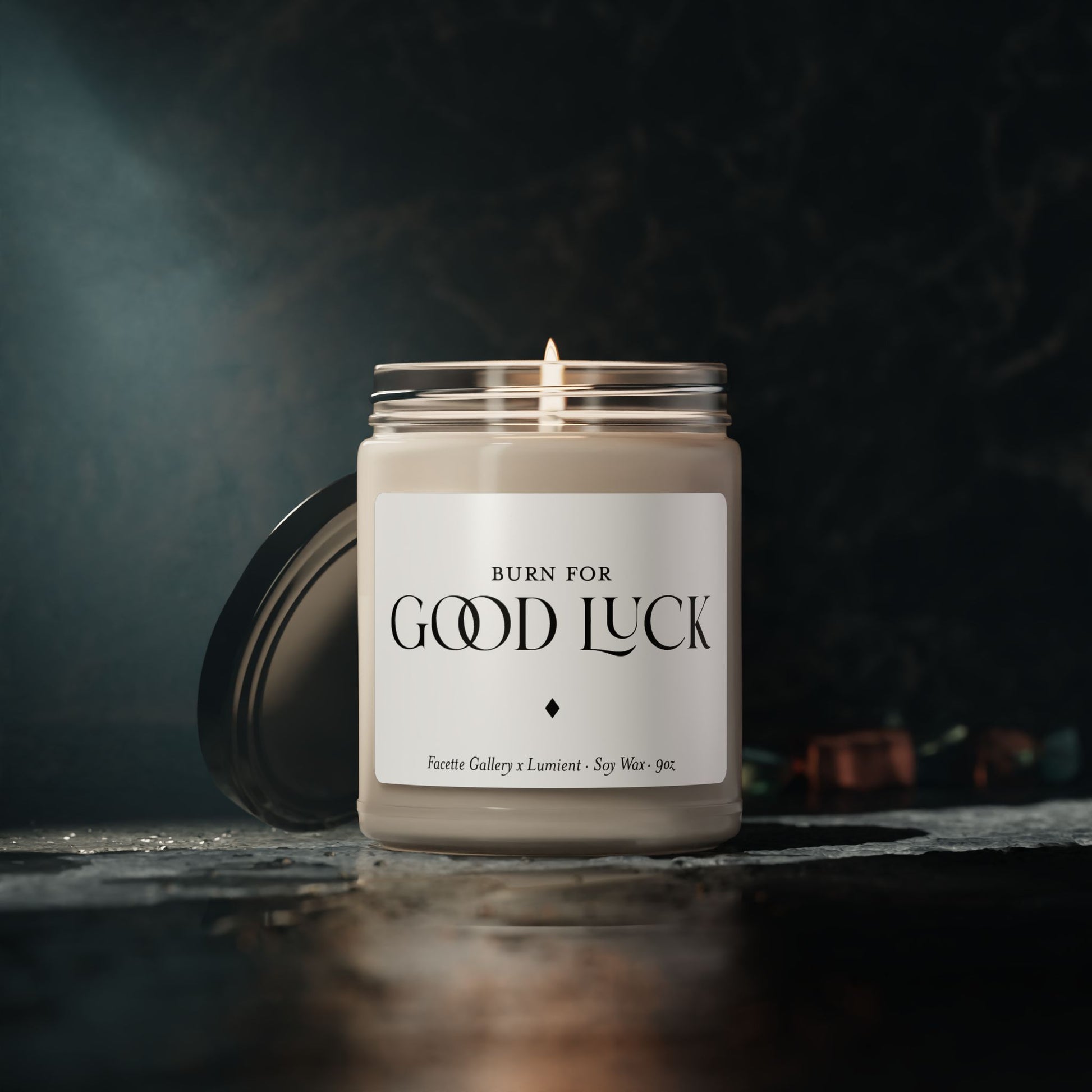 9oz white soy candle in glass jar with black lid, labeled "Burn for Good Luck," lit wick on dark background
