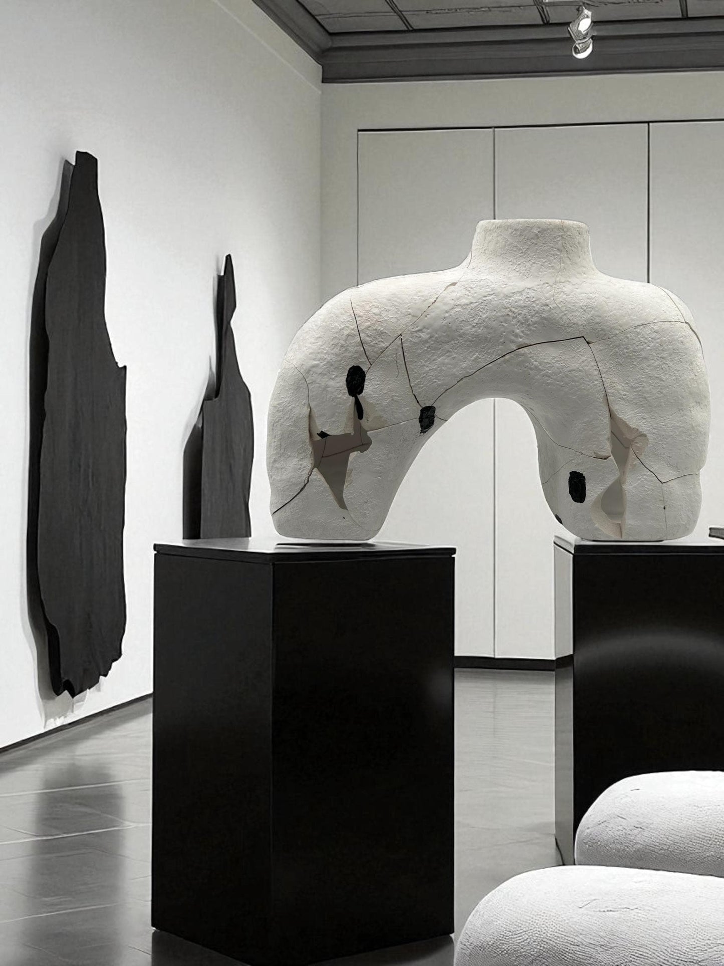 Gallery display of a white broken and repaired abstract Japanese style ceramic sculpture on black pedestal in minimalist room
