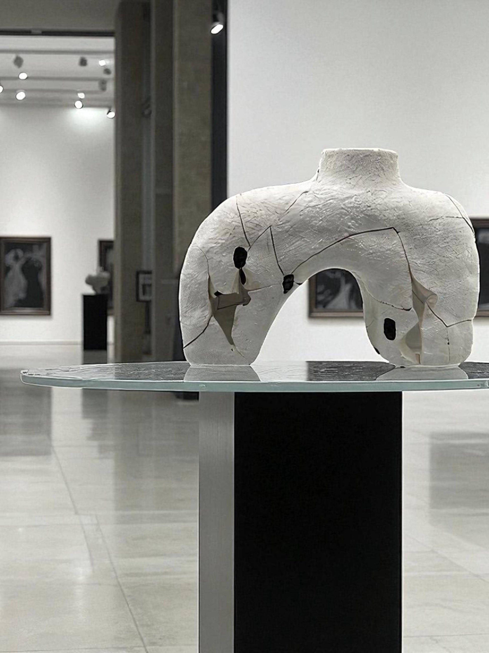 White cracked and repaired Japanese style Hachi vase on glass top pedestal in modern gallery setting