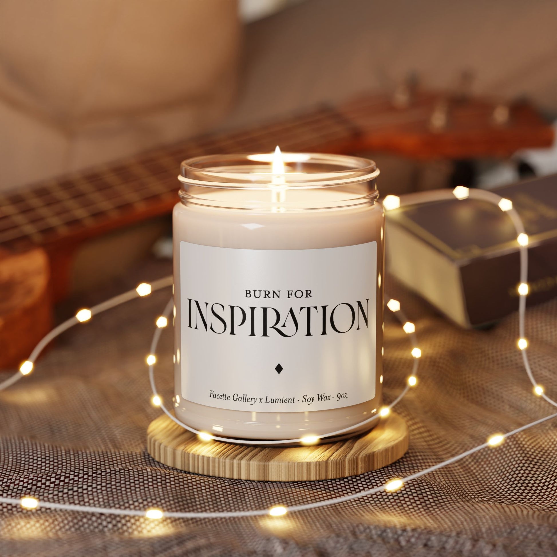 Lit 9oz white soy candle in glass jar with "Burn for Inspiration" label on wooden coaster with fairy lights