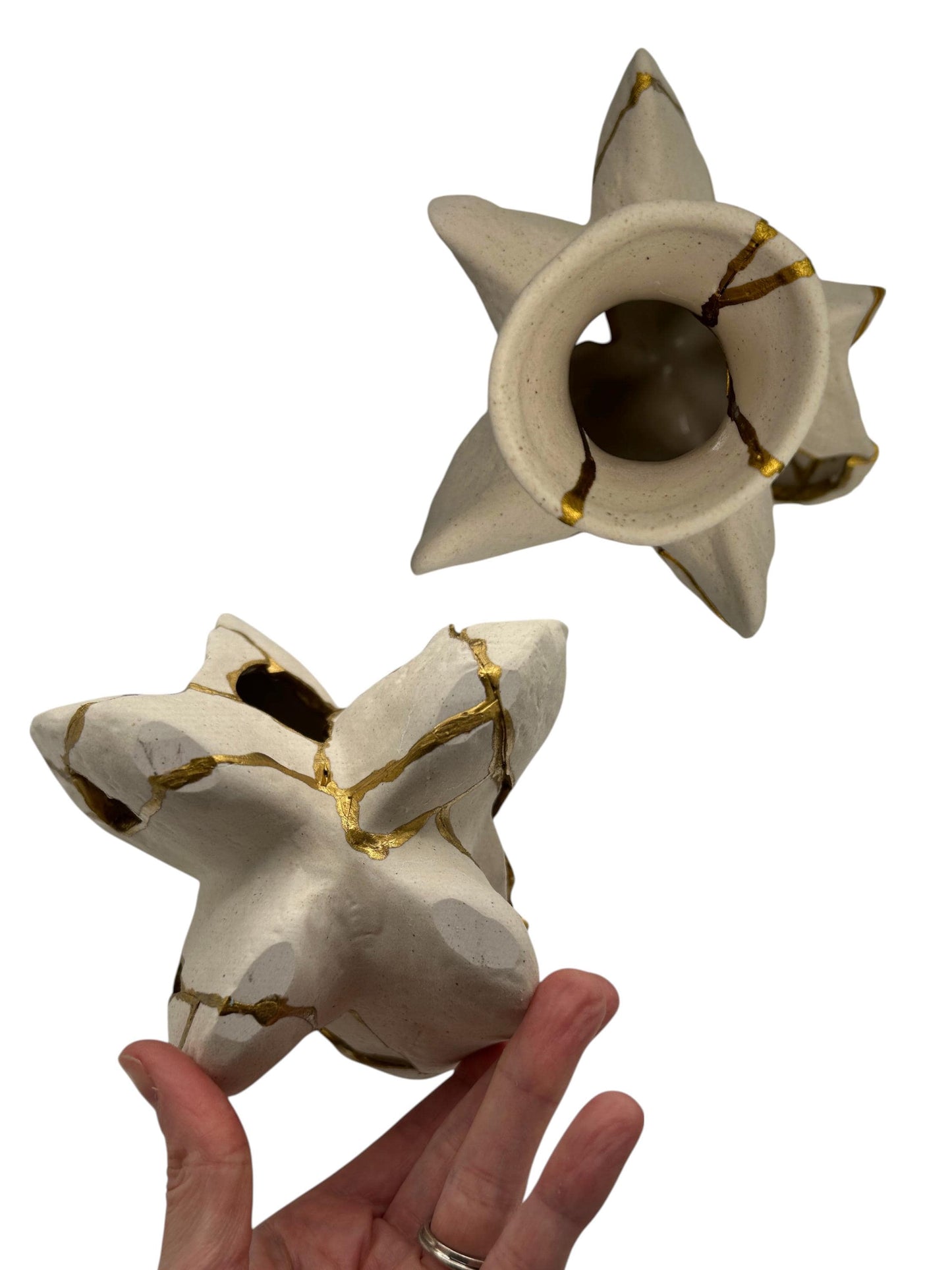 Hand holding modern Kintsugi fossil vase with irregular star shape and gold repaired cracks on ivory pottery surface