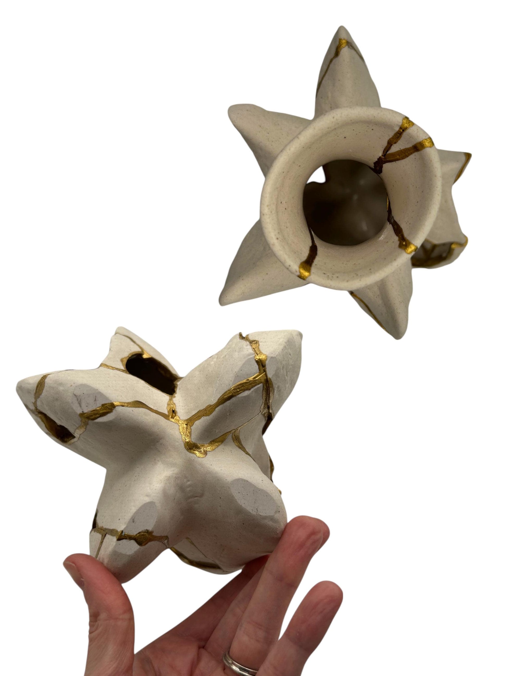 Hand holding modern Kintsugi fossil vase with irregular star shape and gold repaired cracks on ivory pottery surface