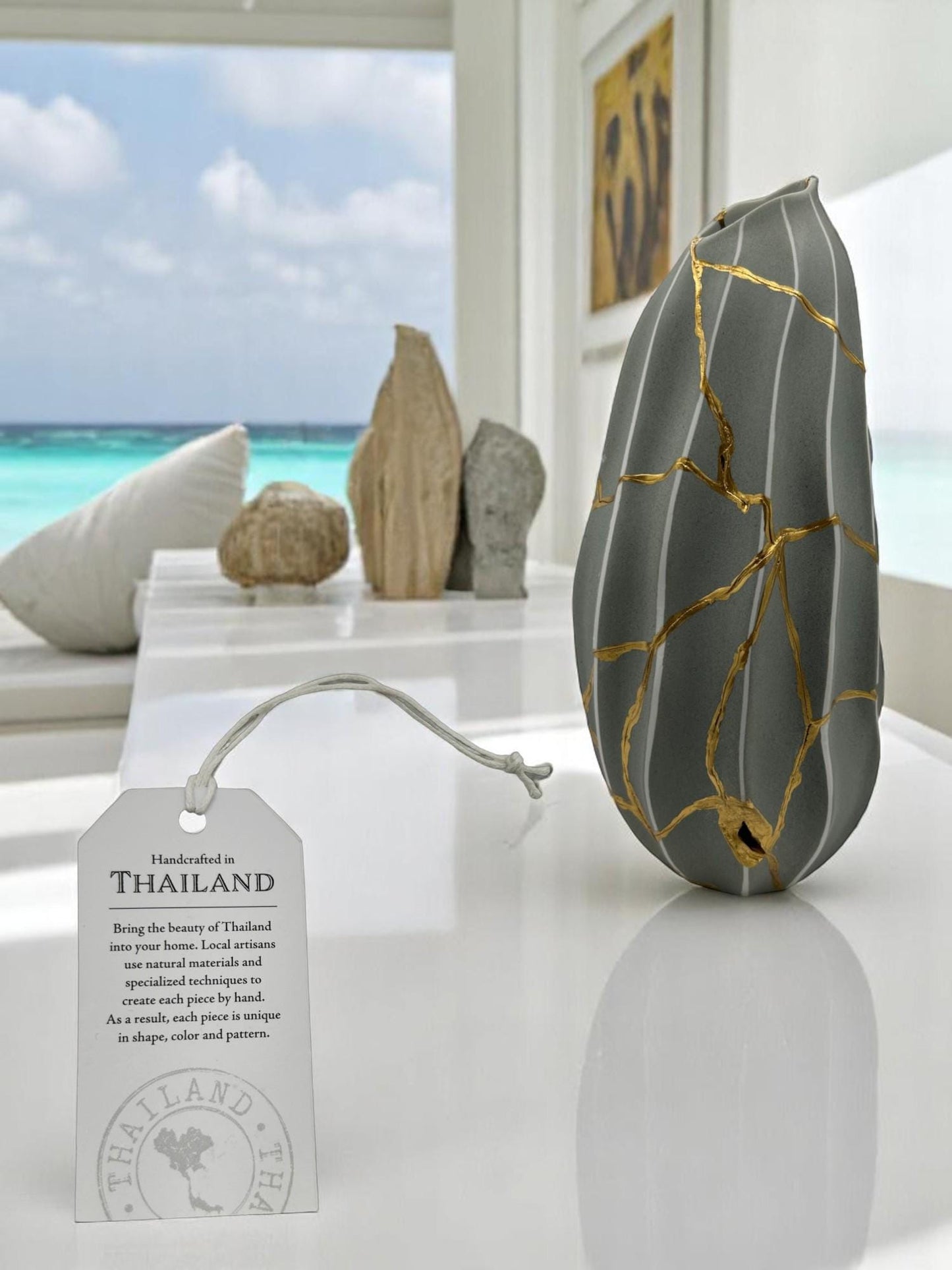Modern gray melon-shaped kintsugi vase with hand-painted gold repairs on white surface in bright room by ocean view