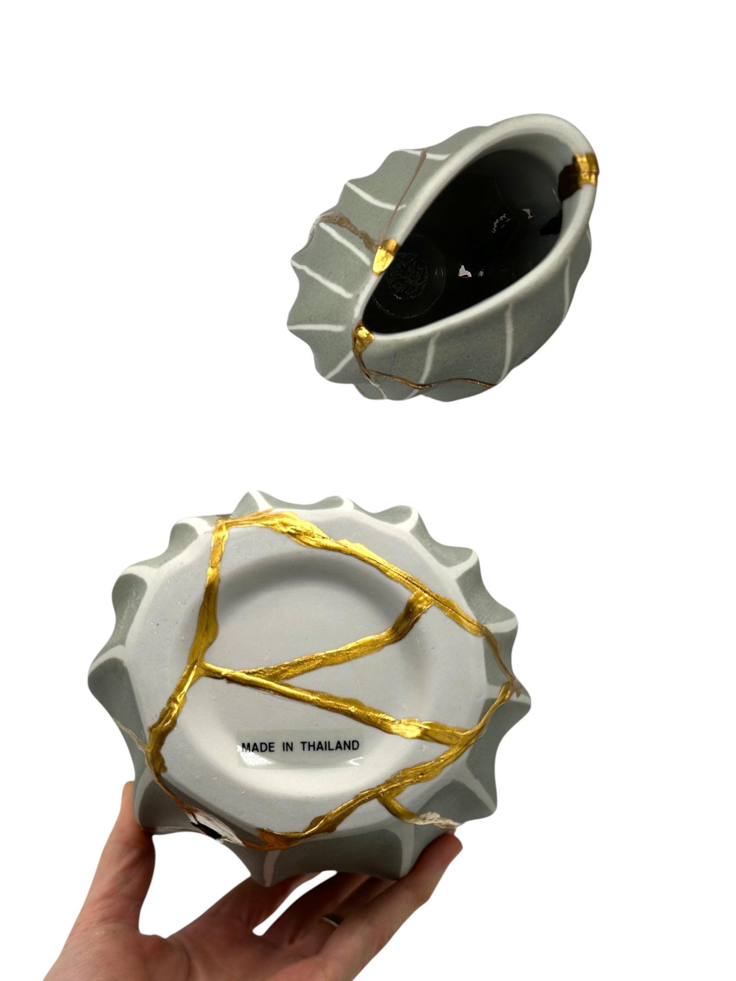 White ceramic melon-shaped vase with gold kintsugi repair lines, held in hand showing bottom marked Made in Thailand