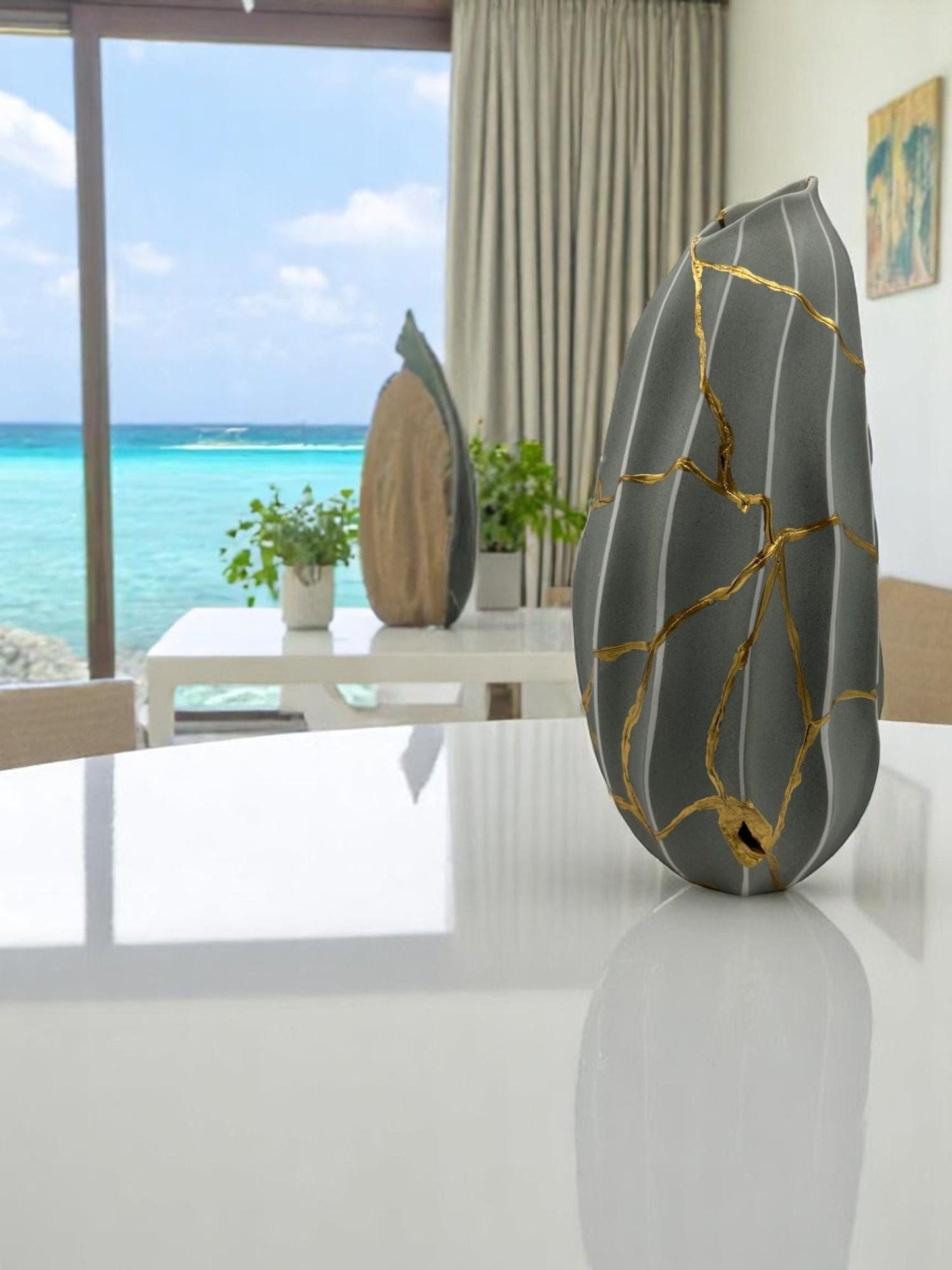 Modern Kintsugi melon-shaped vase in gray with hand-painted gold repair lines, displayed on white table by ocean view window.