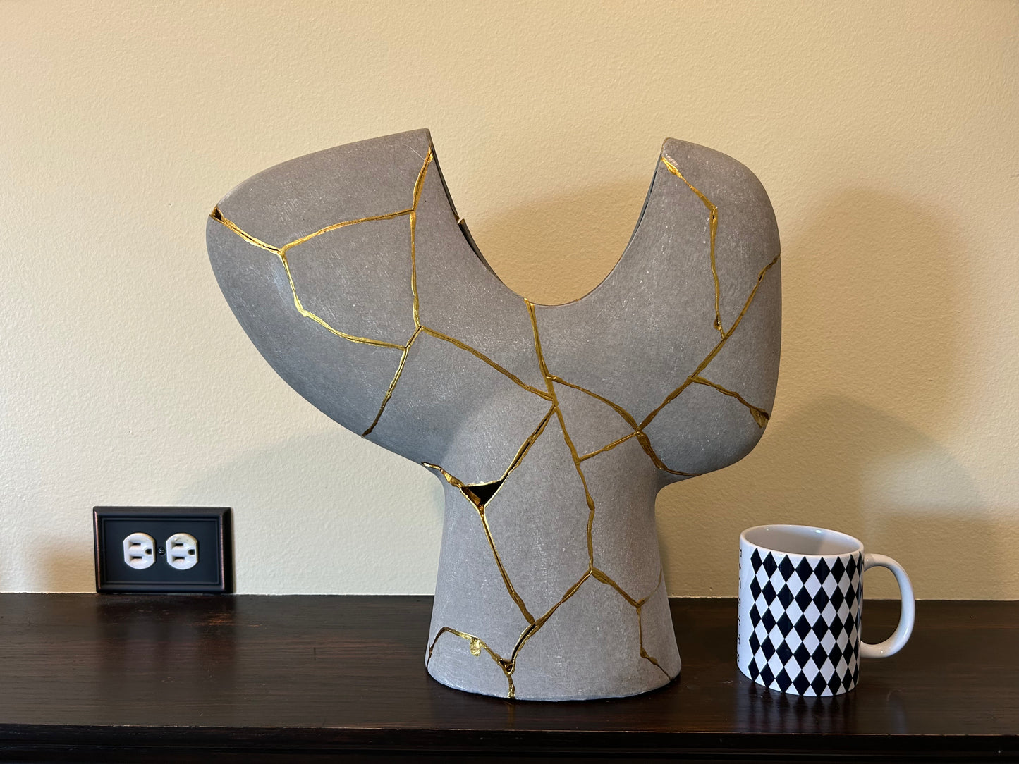 Modern Kintsugi Novak vase in dark gray with hand-painted gold repair lines, displayed next to a white mug with black diamond pattern