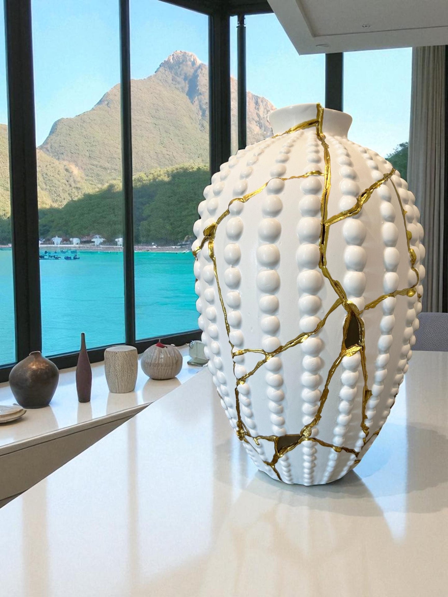 White ceramic Modern Kintsugi Sea Urchin Vase with hand-painted gold repair lines on glossy surface by window with mountain view