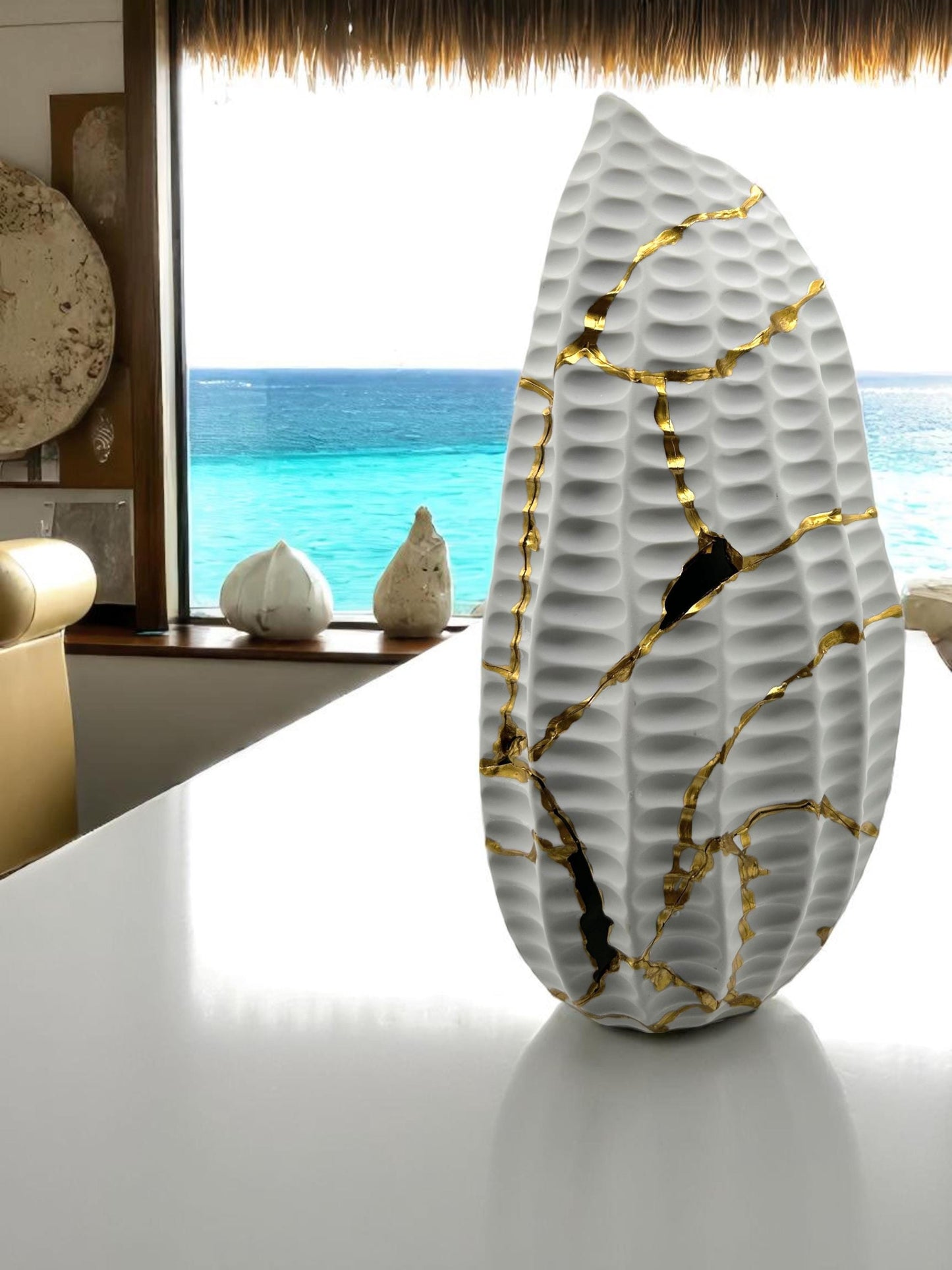 Modern white kintsugi seahorse vase with gold hand-painted repairs, textured surface, displayed by ocean view window