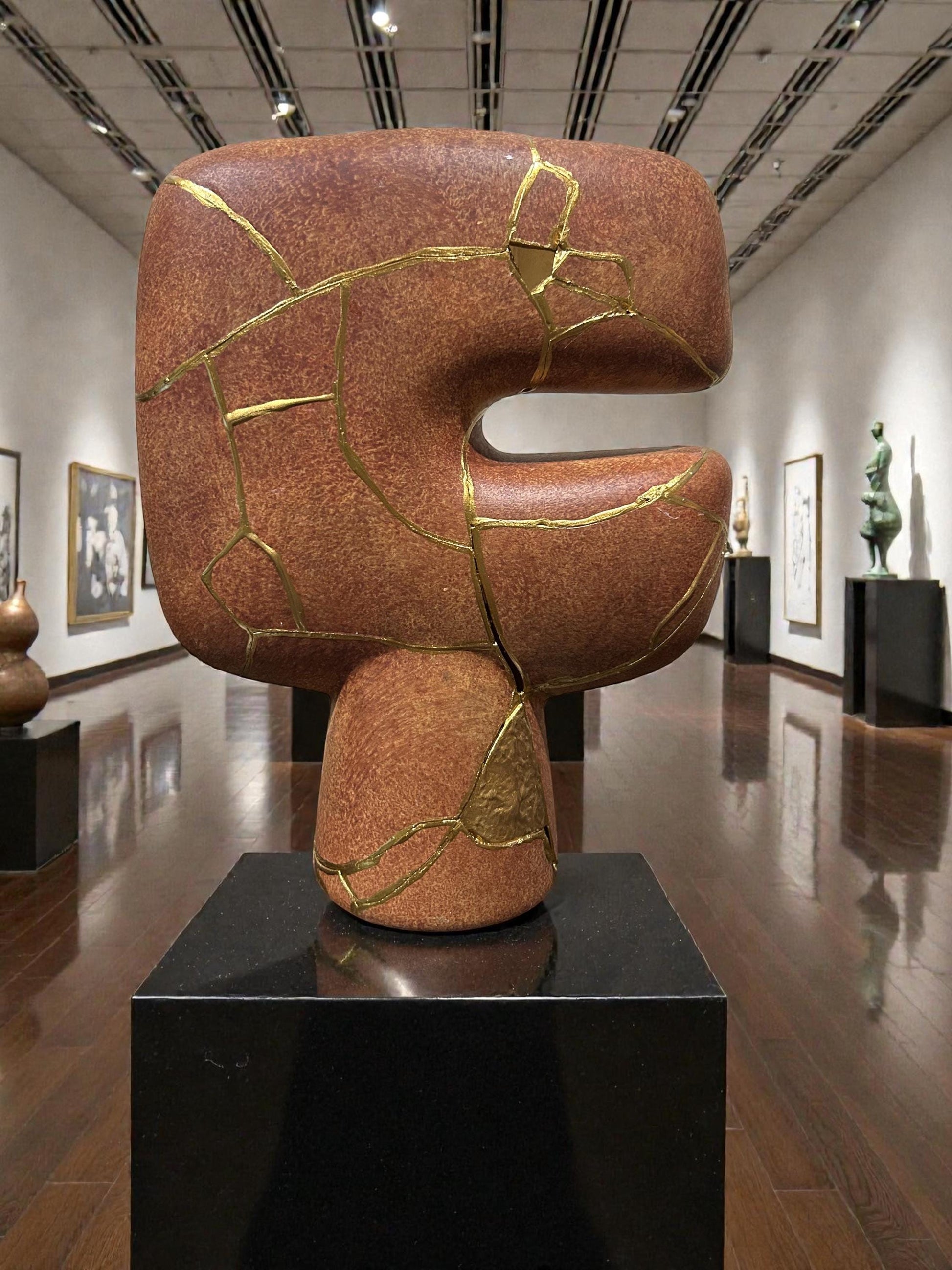 Modern brown kintsugi vase with gold hand-painted repairs, abstract shape, displayed in art gallery setting.