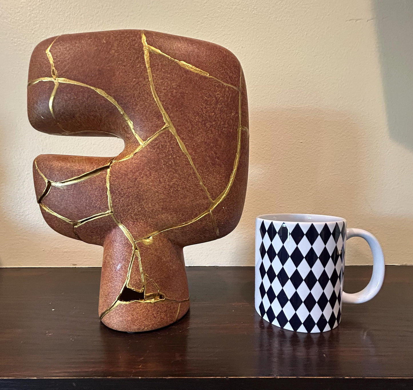 Modern brown kintsugi vase with hand-painted gold repair lines, abstract tribal design, next to black and white diamond mug