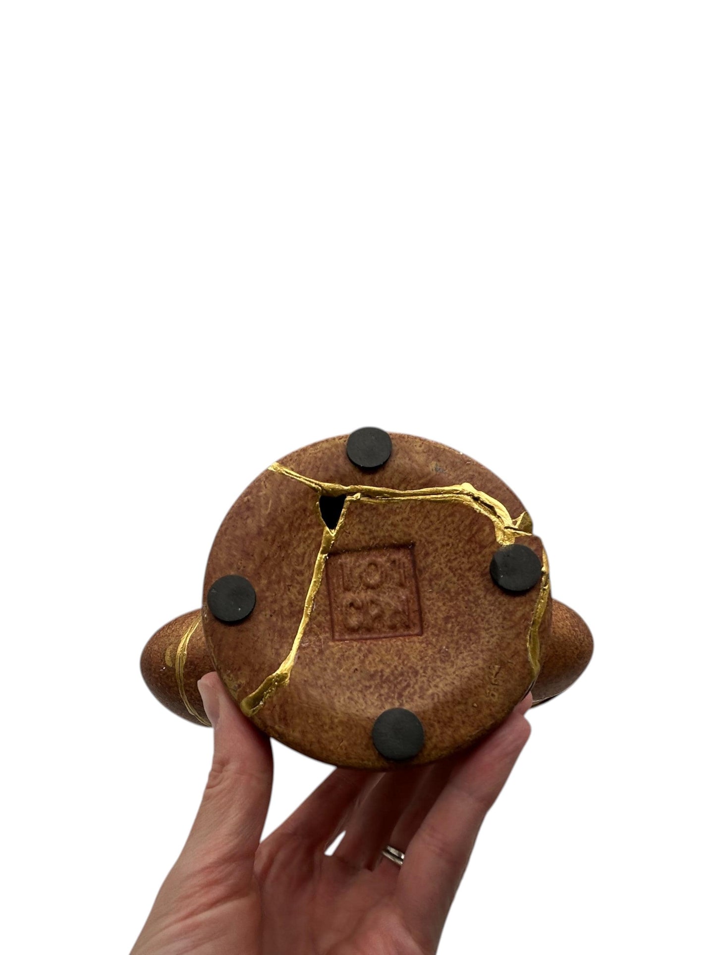 Hand holding bottom of brown kintsugi vase with visible gold repairs and black protective pads on white background