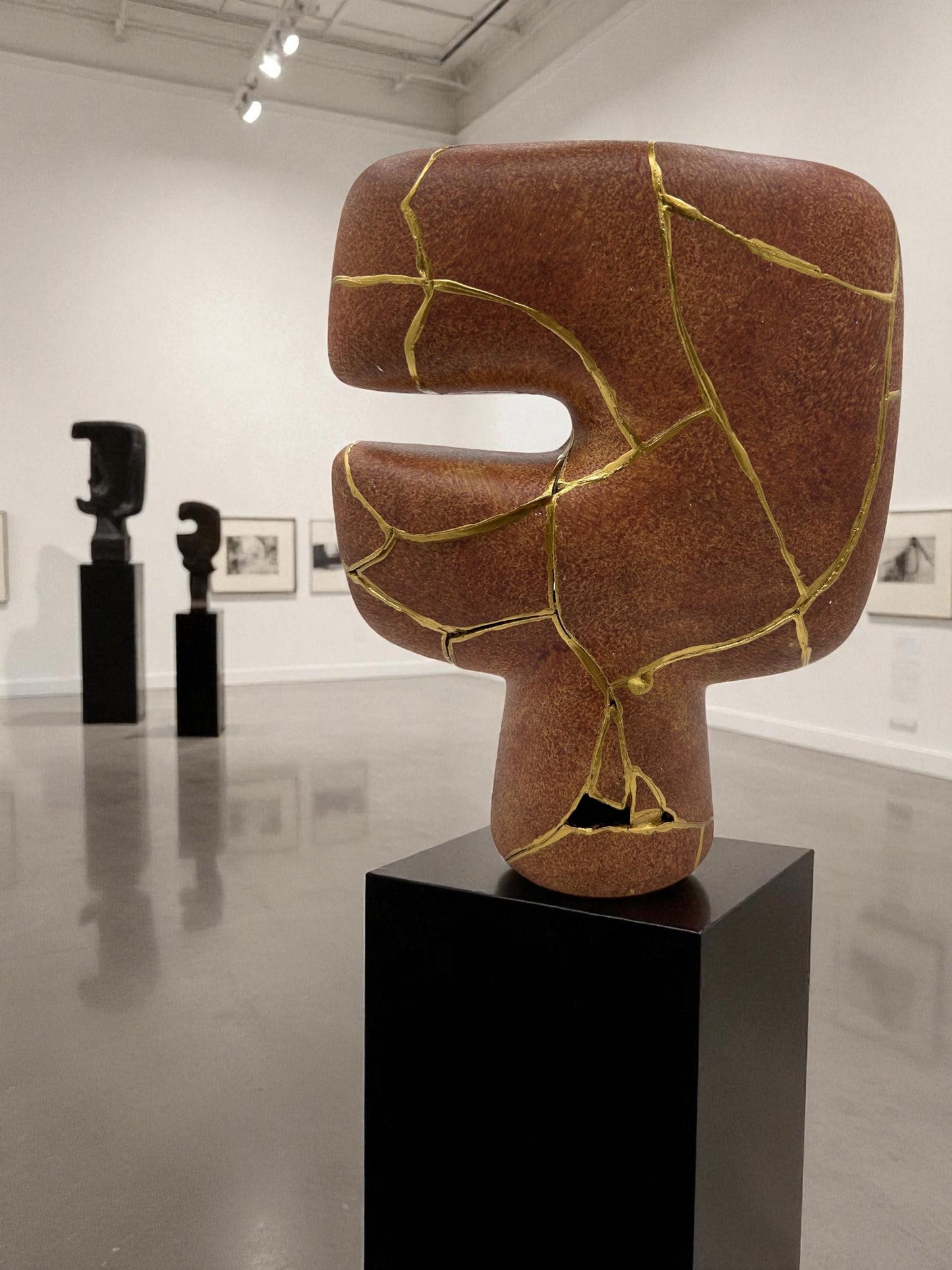 Handcrafted modern kintsugi tribal vase with gold repairs on brown pottery, displayed on black pedestal in gallery setting