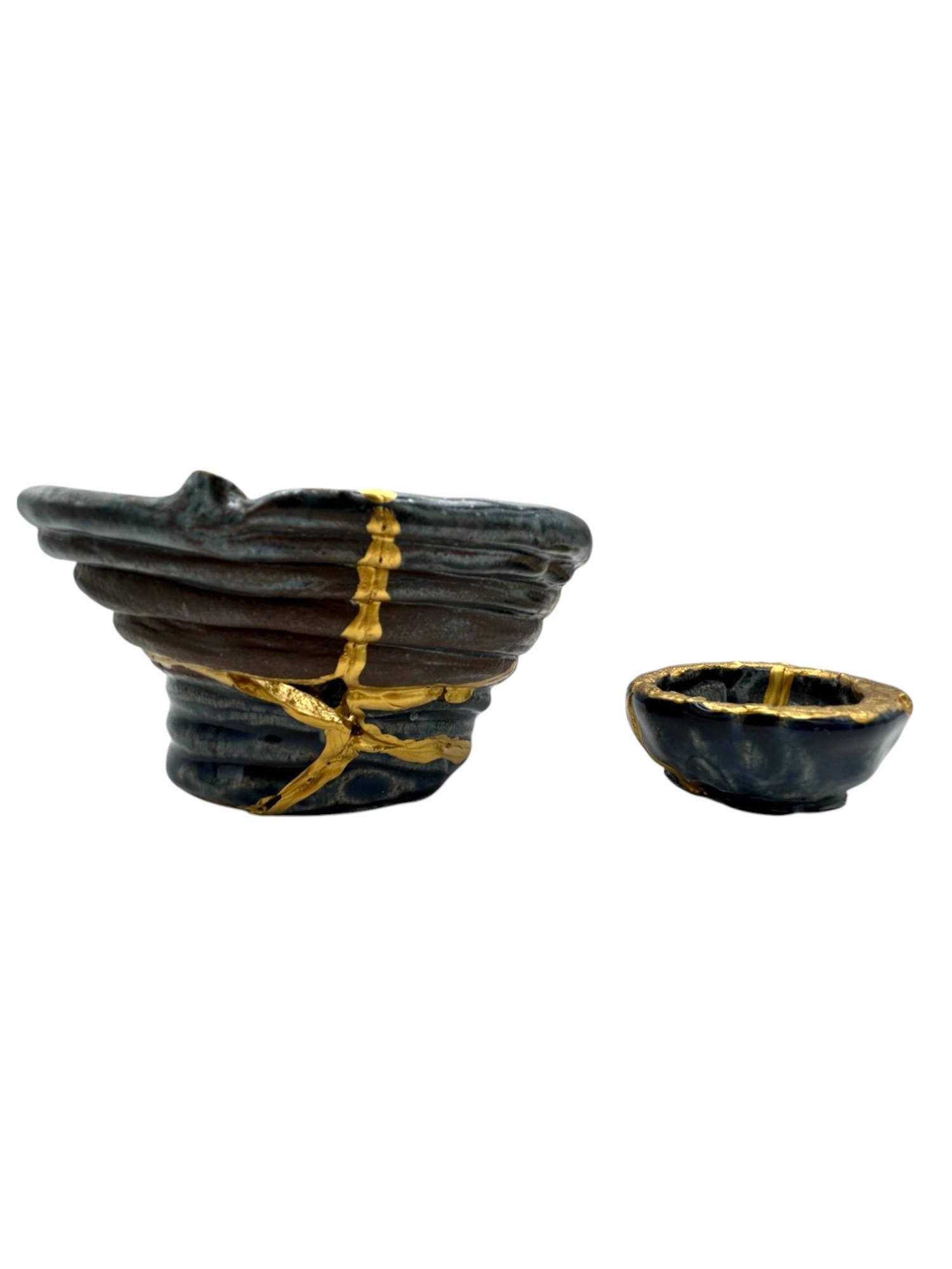 Two-piece set of modern kintsugi style black ceramic bowls with hand-painted gold repair accents on white background