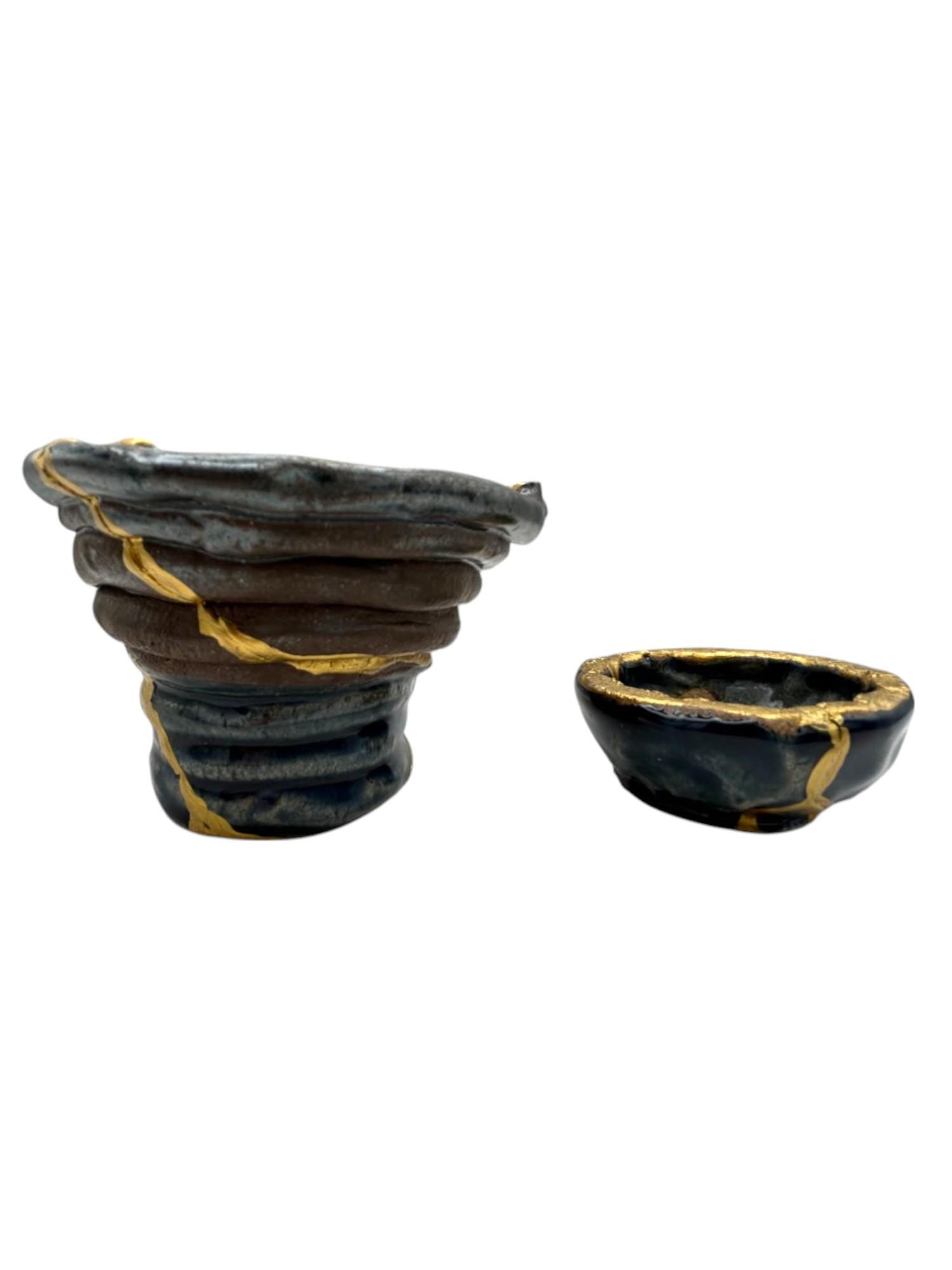 Two-piece set of modern Kintsugi ceramic bowls with hand-painted gold repair lines on dark blue pottery.