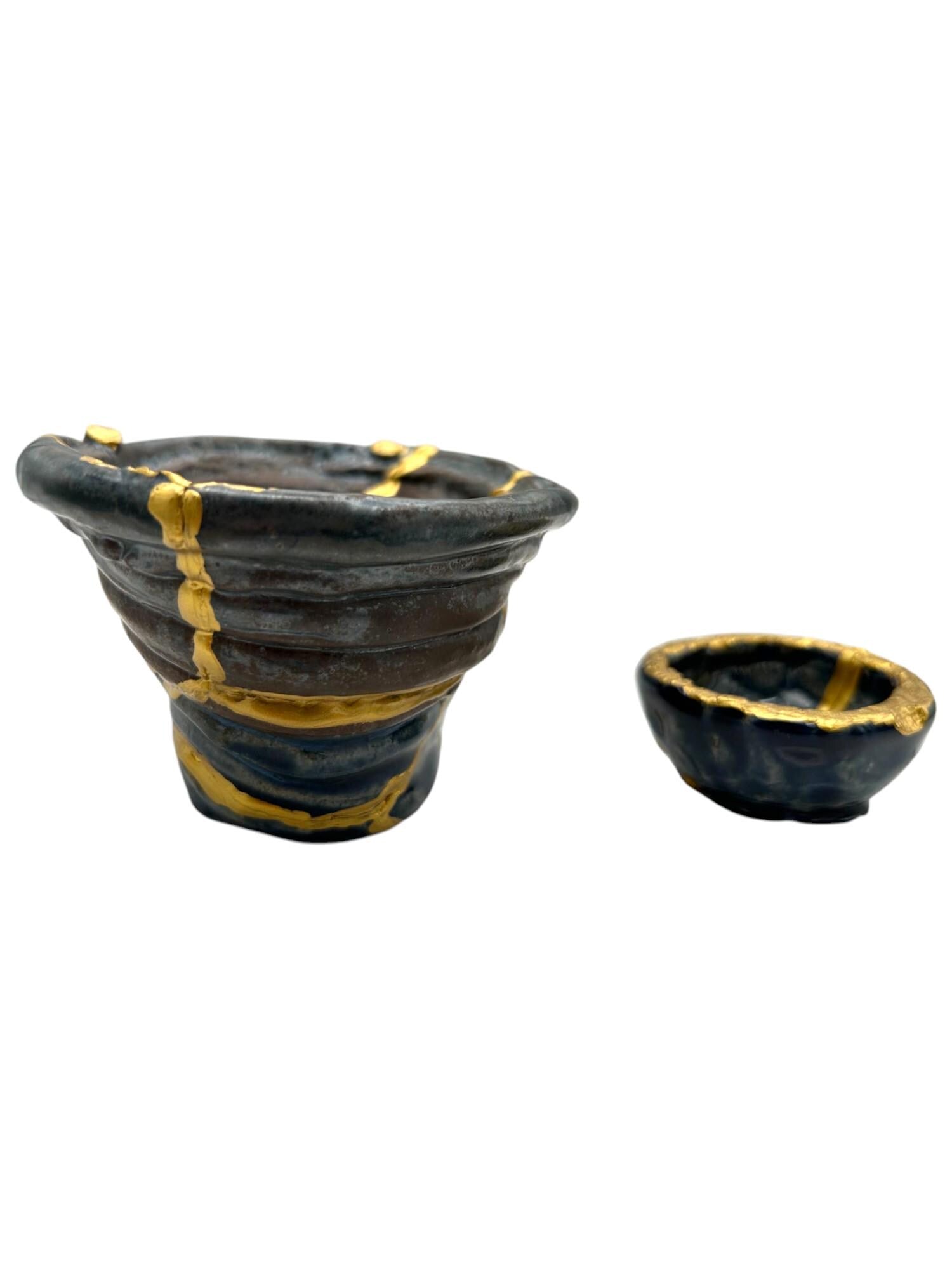 Two-piece set of modern black ceramic Kintsugi bowls with hand-painted gold repairs on white background