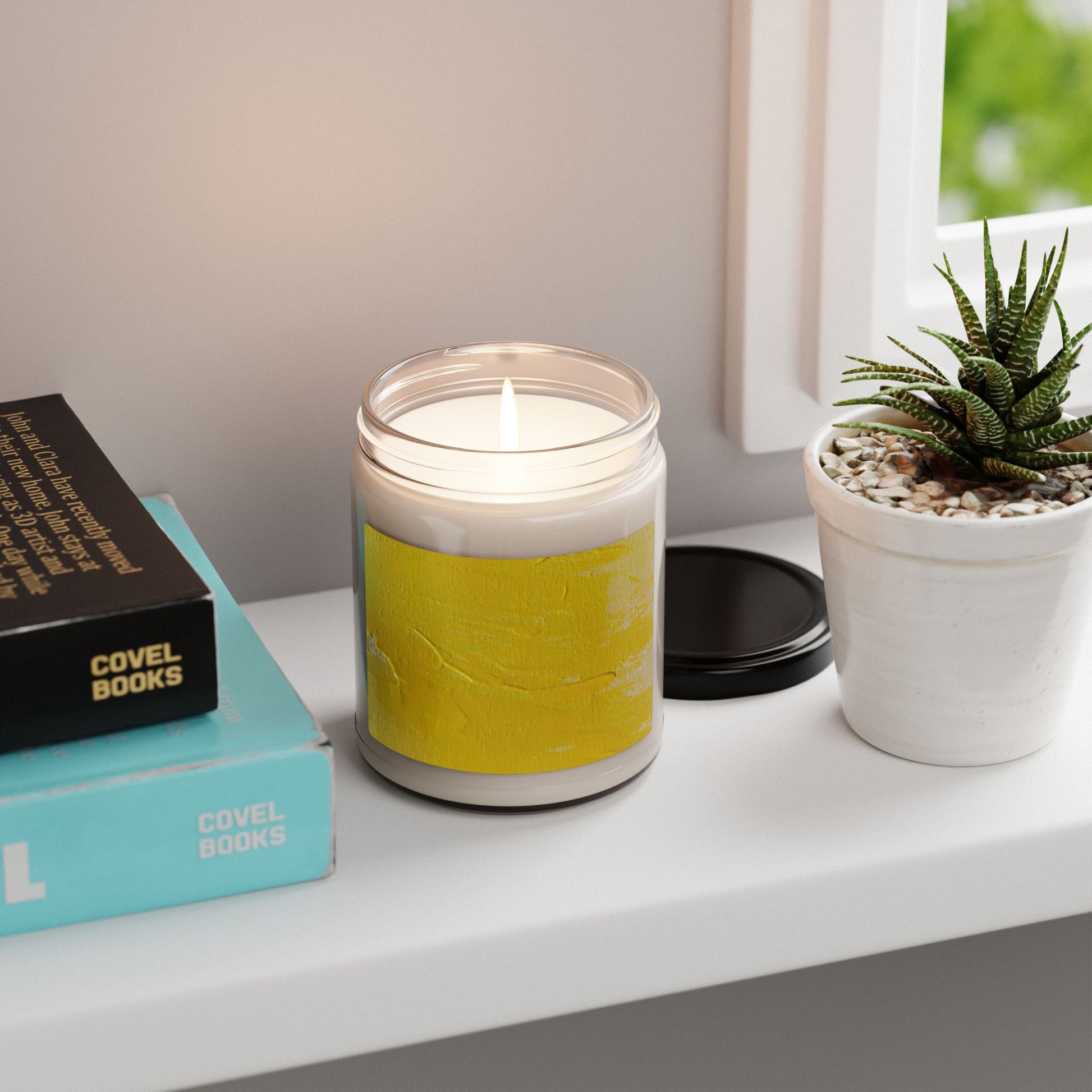 Lit Moment in Yellow soy candle in 9oz glass jar with abstract yellow label, on white shelf near potted succulent and books