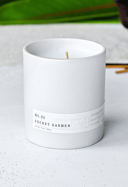 White ceramic candle labeled No. 51 Secret Garden with single wick on light textured surface background