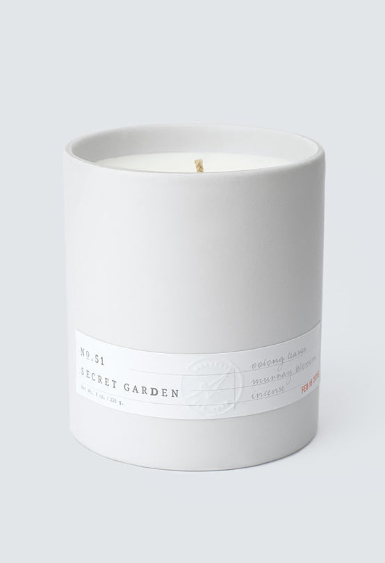 No. 51 Secret Garden scented candle in a simple white ceramic container with minimalist label on light gray background