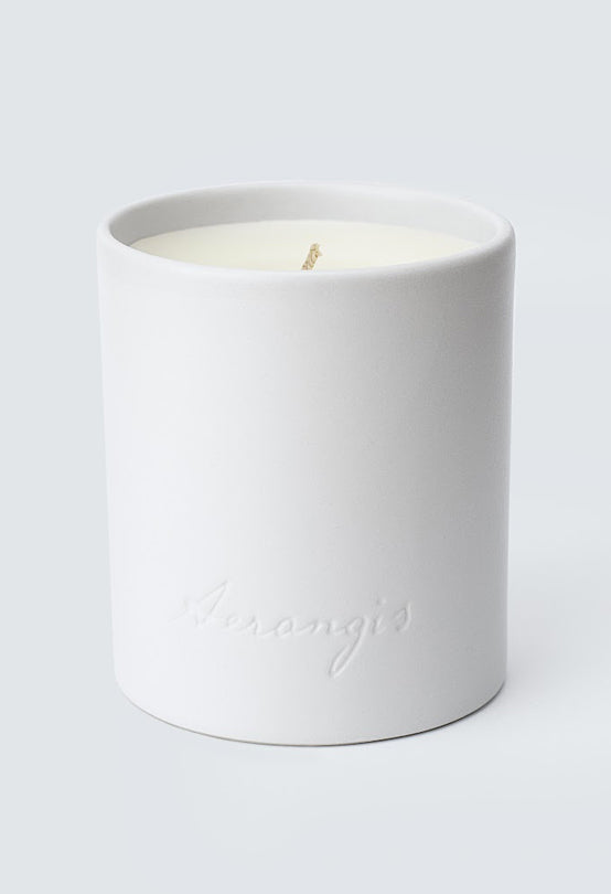 White ceramic candle holder with subtle engraved logo, filled with a single wick candle on light gray background