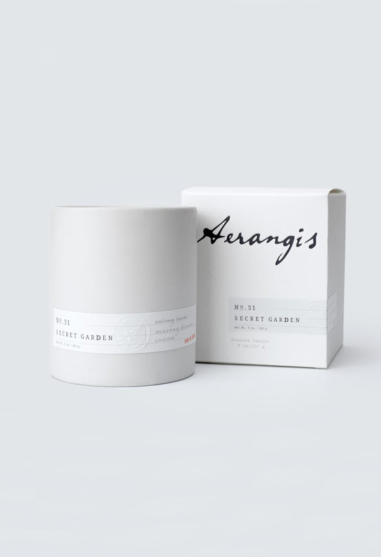 White ceramic candle container with No. 51 Secret Garden label next to matching white packaging box on gray background
