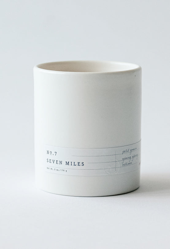 White ceramic candle holder with No.7 Seven Miles label featuring floral scent notes on light grey background
