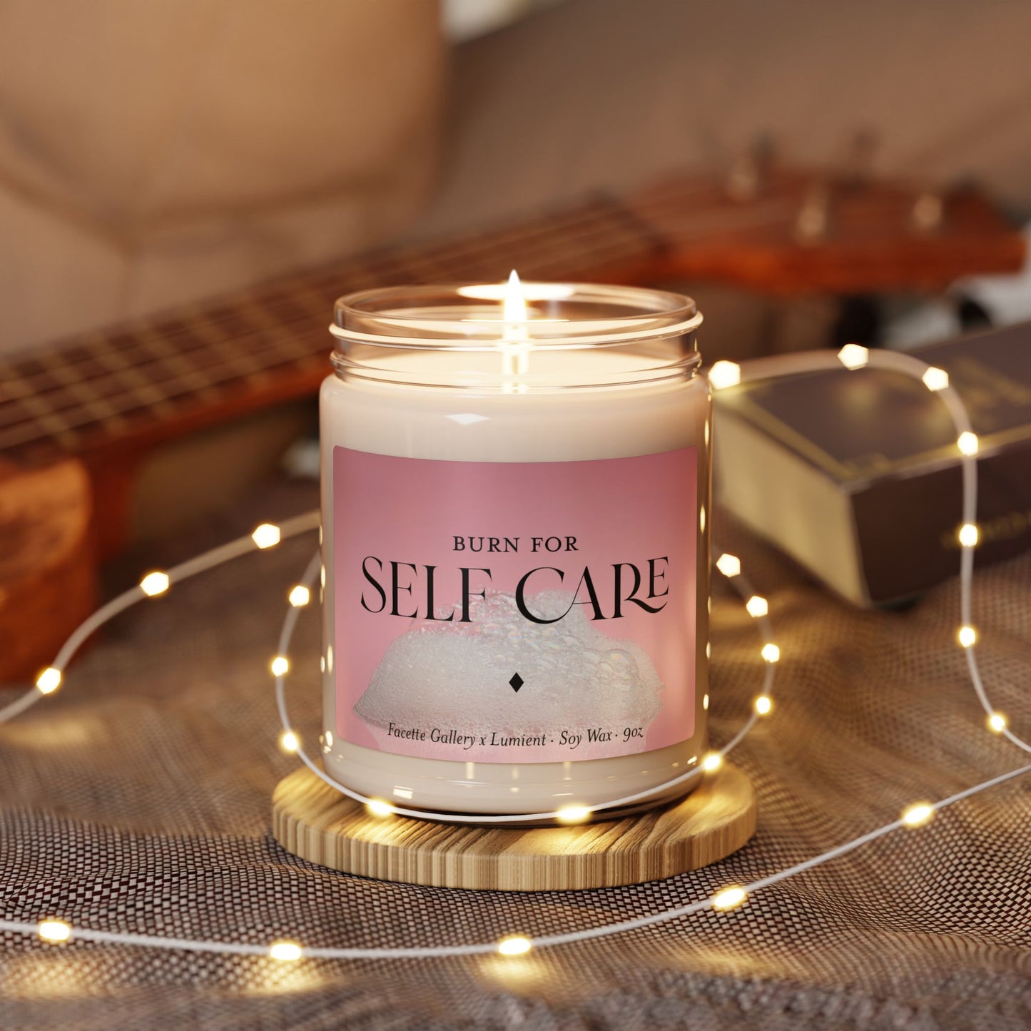 Lit 9oz soy self care candle in glass jar with pink bubble bath label on wooden coaster surrounded by fairy lights