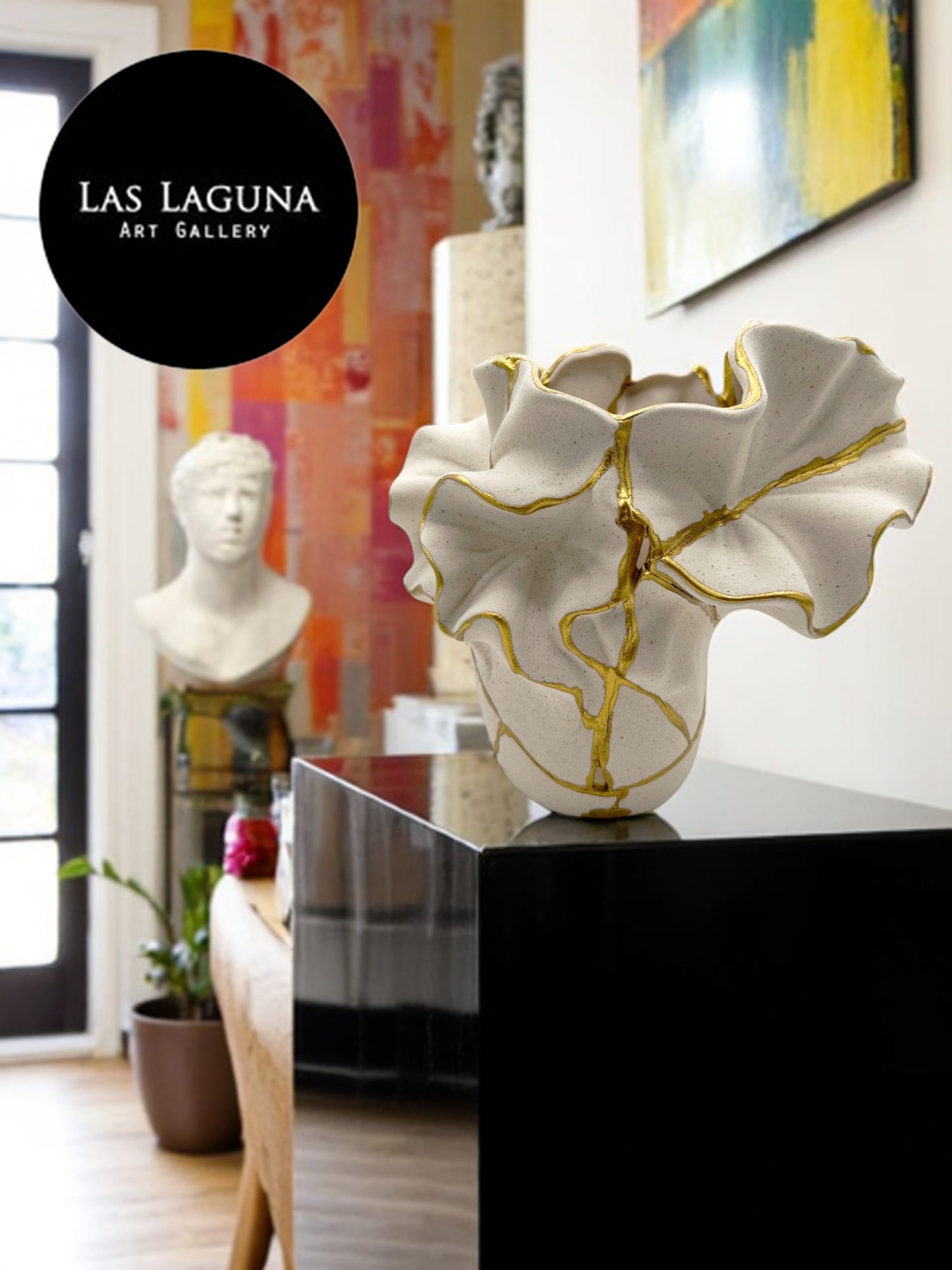 White ceramic vase with ruffled edges and gold metallic cracks displayed on black pedestal in gallery setting